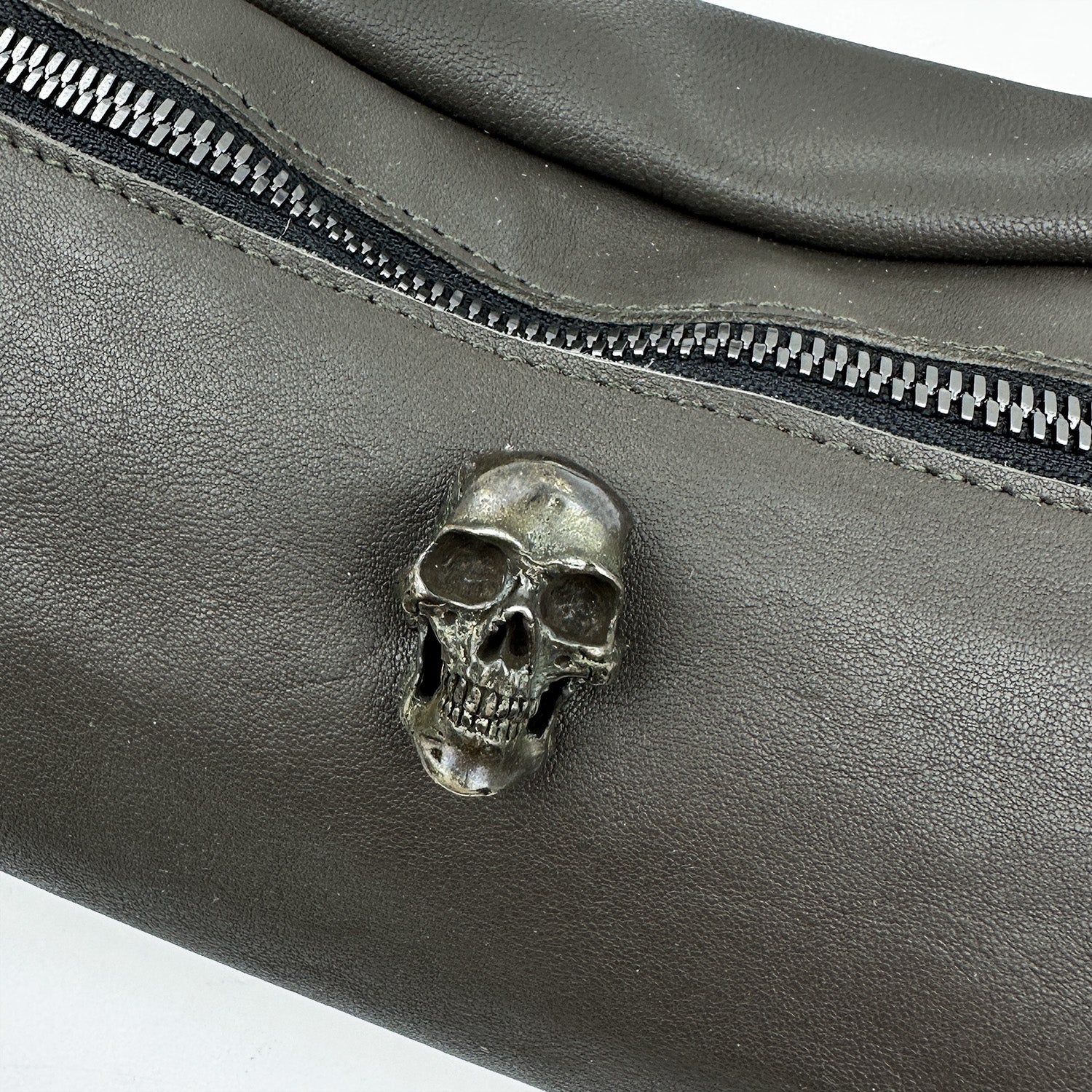 Close-up of the STELLA - OLIVE-GREY crossbody bag from evokewomen, featuring black leather with a silver skull embellishment above a zipper.