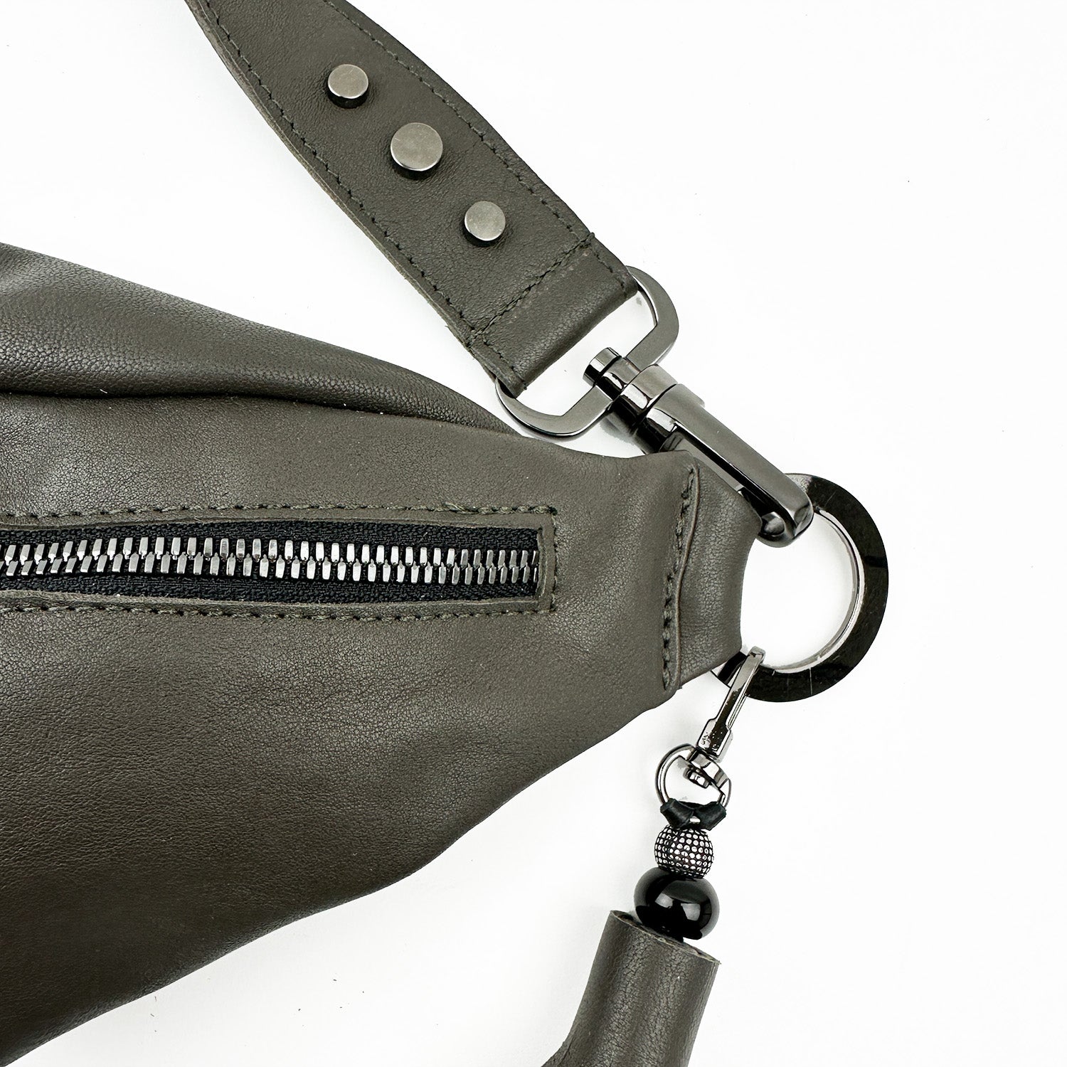 Close-up of the STELLA - OLIVE-GREY leather crossbody bag by evokewomen, showcasing a black zipper, metal ring, and decorative beads on the handle.