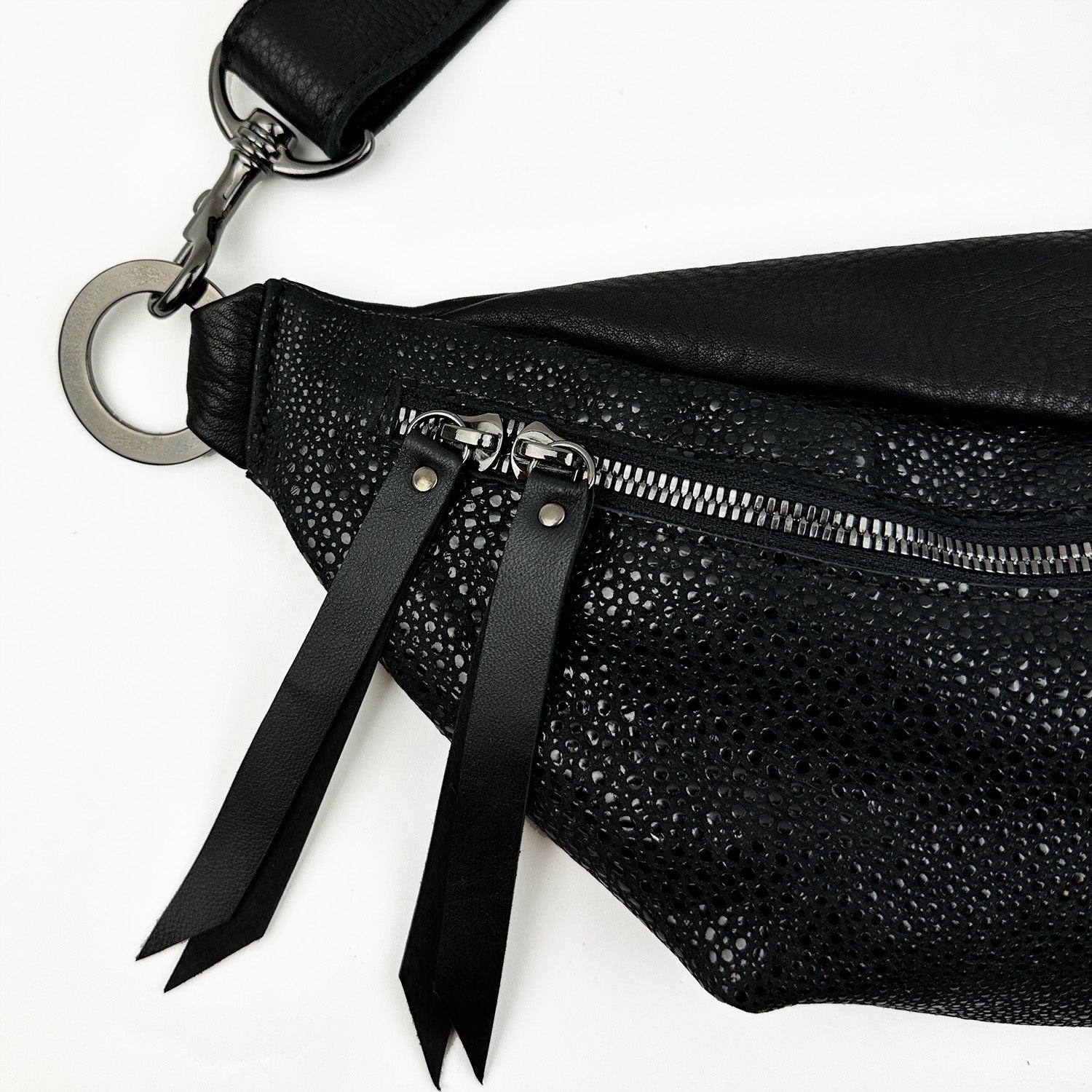Detailed view of the STELLA - BLACK STINGRAY, featuring a textured faux stingray leather finish by evokewomen, equipped with two zipper pulls and a large metal ring on the strap, ideal for a sleek cross body bag style.