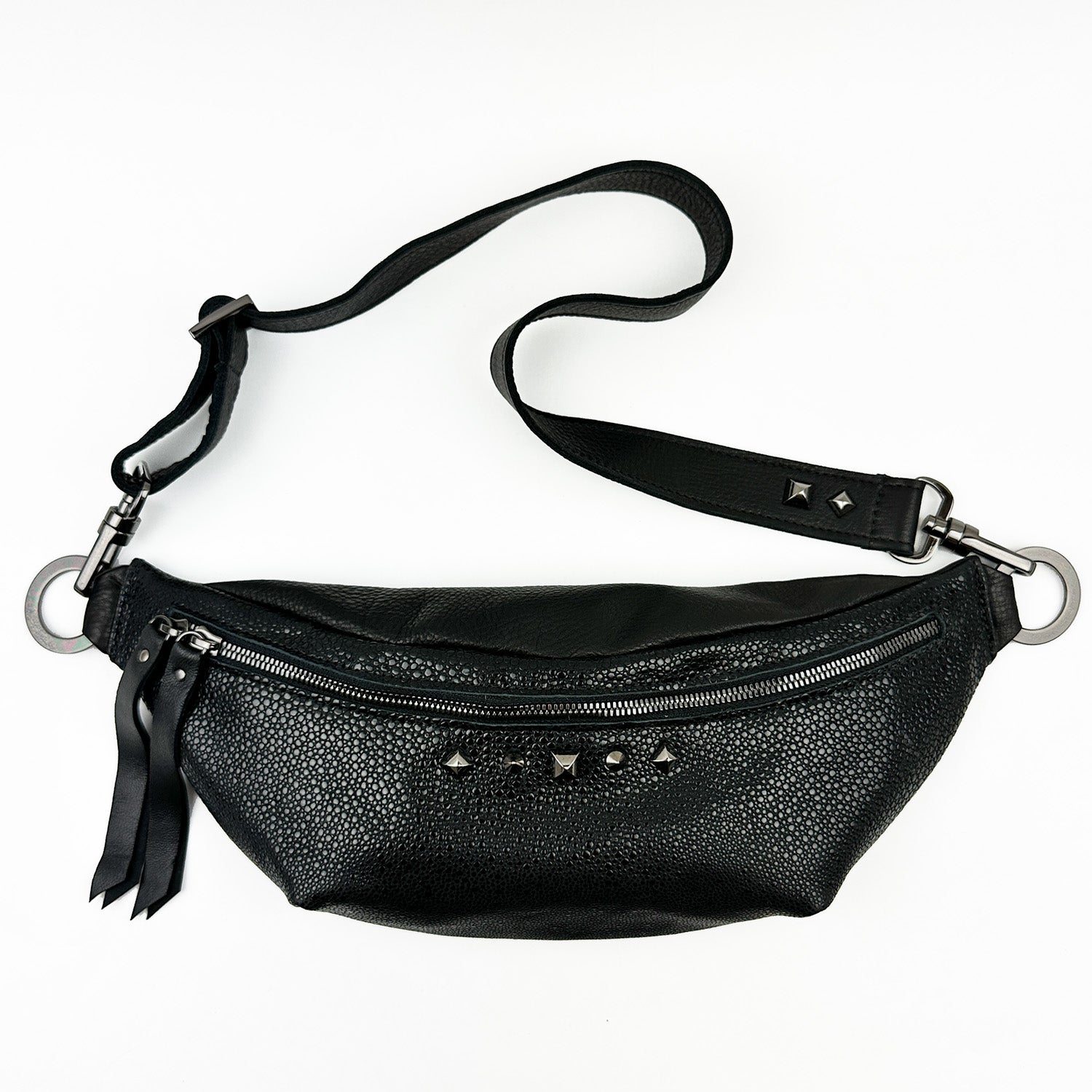 The STELLA - BLACK STINGRAY by evokewomen is a stylish sling bag, crafted with a textured faux stingray leather finish. It features a front zipper, decorative studs, and an adjustable strap for versatile styling.