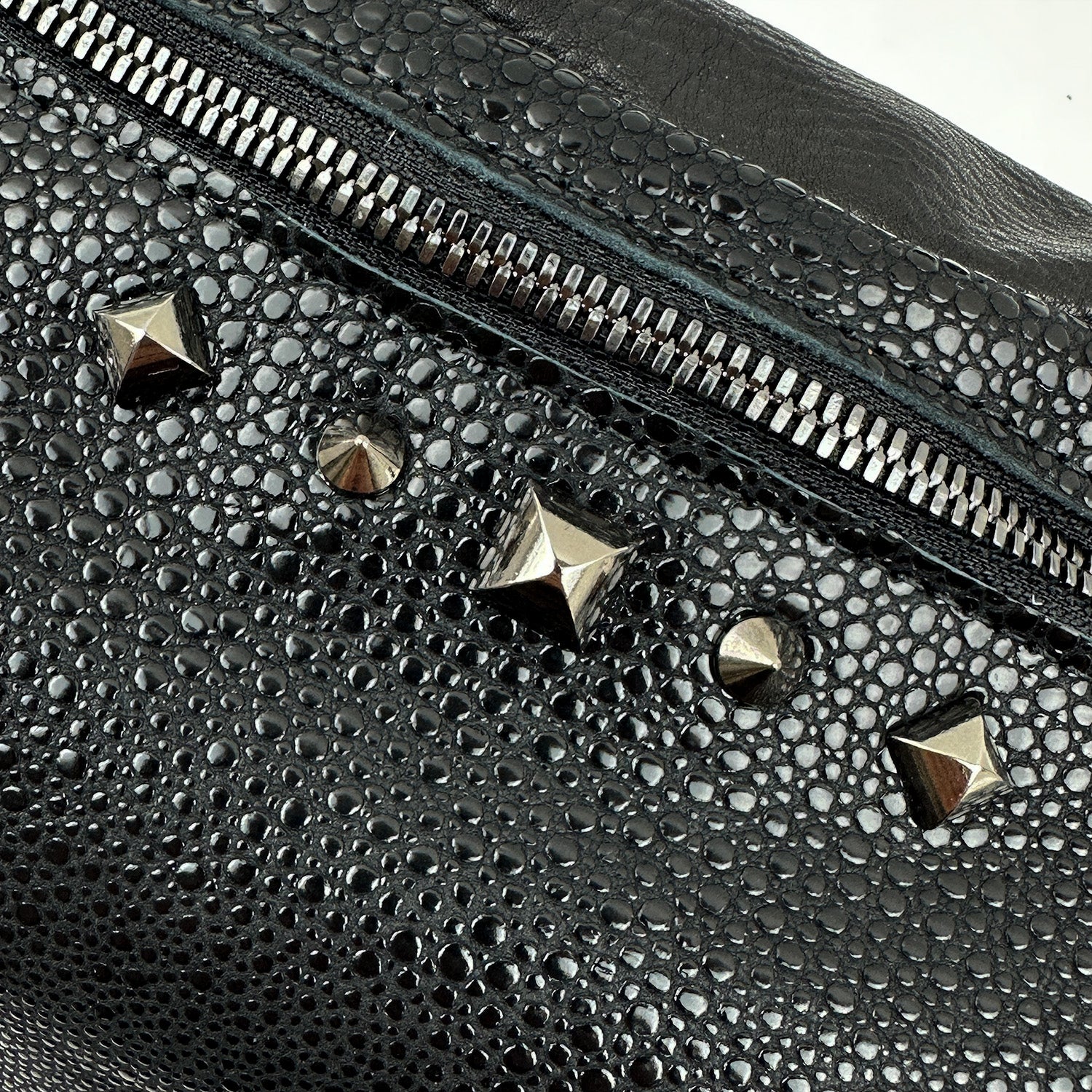 Close-up of the STELLA - BLACK STINGRAY sling bag by evokewomen, featuring textured faux stingray leather, a silver zipper, and metallic stud accents.