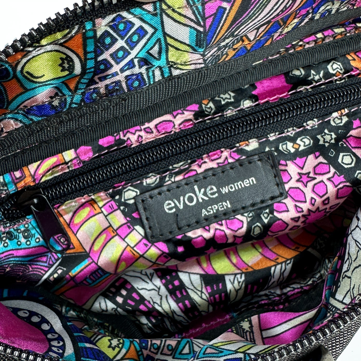 Close-up of the inside of a colorful patterned crossbody bag reveals a label that reads "evokewomen STELLA - GUNMETAL TEXTURE.