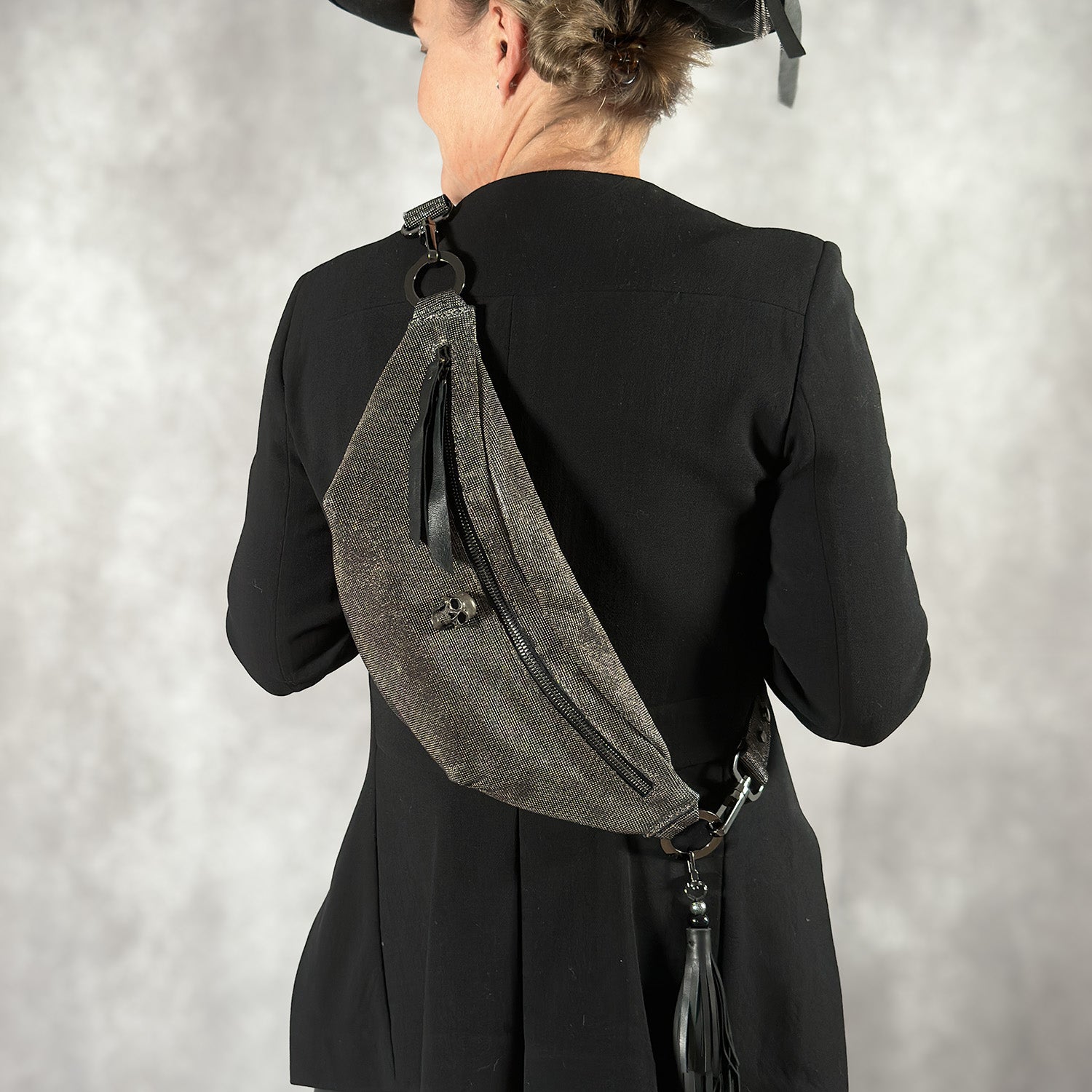 A person in a black outfit and hat is shown from the back, wearing the stylish STELLA - GUNMETAL TEXTURE sling bag by evokewomen over the shoulder.