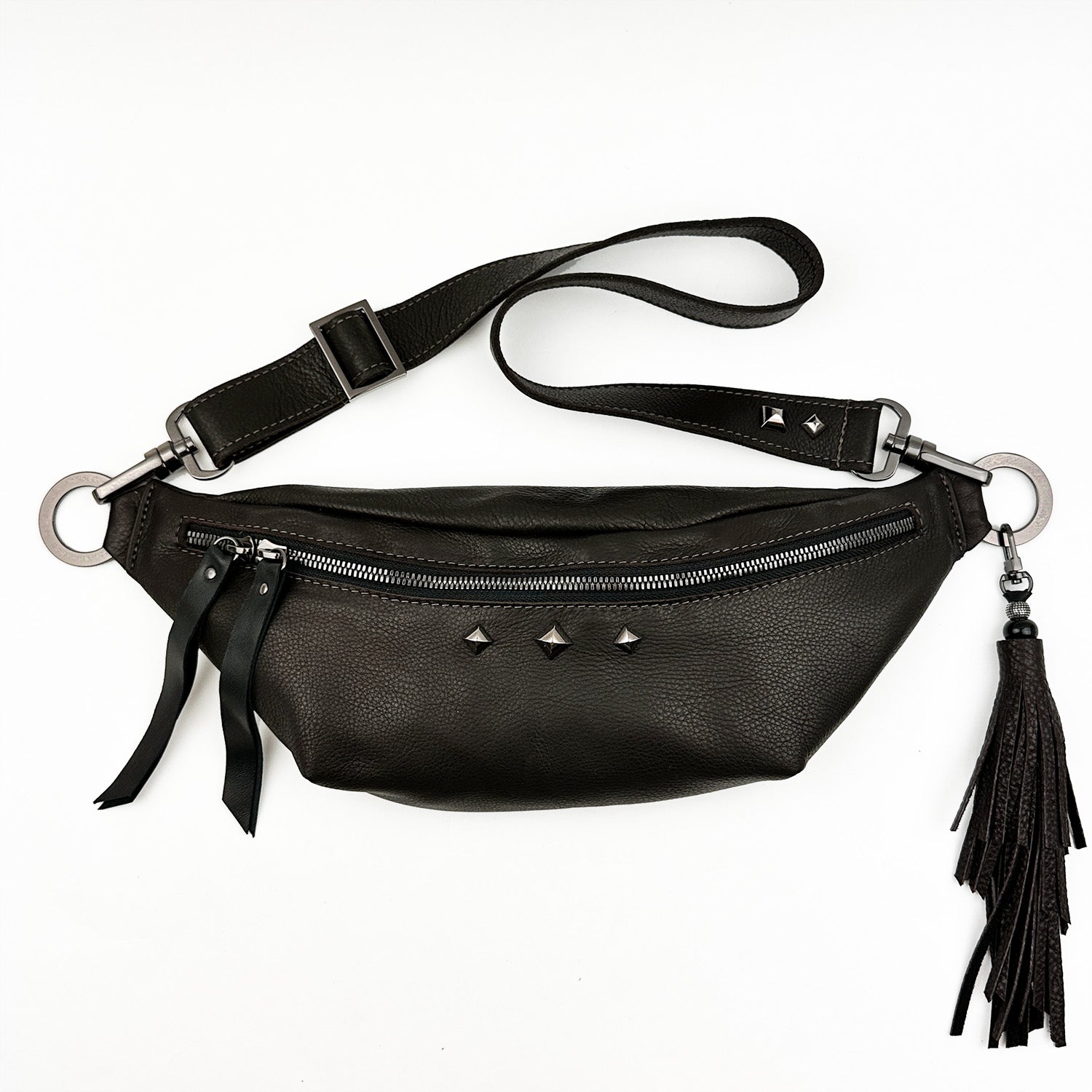 The STELLA - BROWN belt bag by evokewomen boasts a sleek design made from Italian leather, featuring a front zipper, metal studs, and an adjustable strap adorned with a decorative tassel.