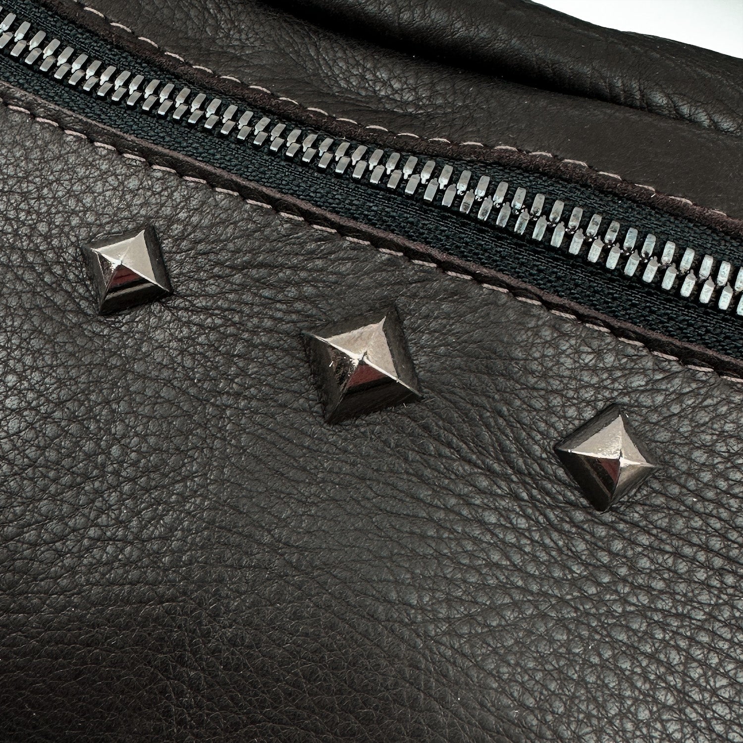 Close-up of the STELLA - BROWN by evokewomen, a sleek sling bag crafted from Italian leather, featuring a zipper, metal stud accents, and an adjustable strap for comfort.