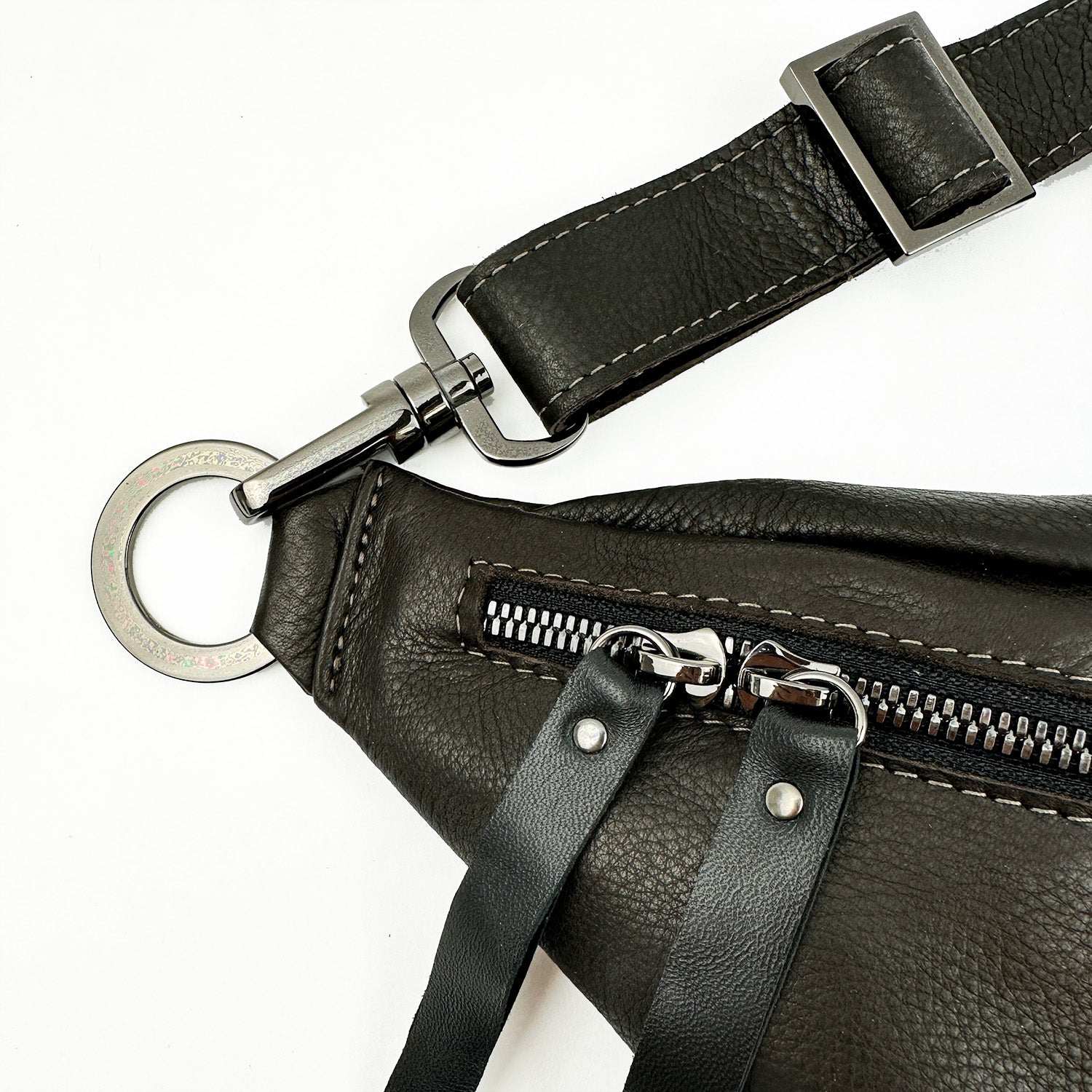 Close-up of the STELLA - BROWN sling bag by evokewomen, crafted from black Italian leather with a silver zipper and metal ring. The adjustable strap includes a sleek buckle for both comfort and style.