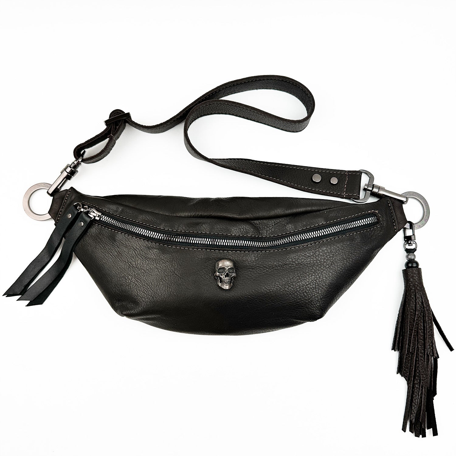 The STELLA - BROWN sling bag by evokewomen is crafted from luxurious Italian leather and features a central zipper adorned with a prominent skull decoration, along with long, fringed tassels on the sides.
