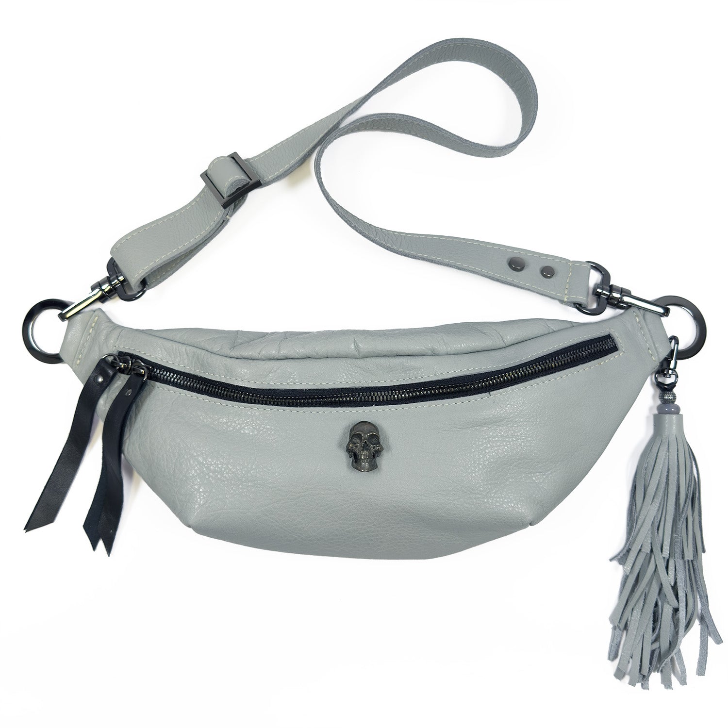 The STELLA - light smoke by evokewomen is a gray leather crossbody sling bag featuring an adjustable strap, black zipper, skull embellishment, and a long tassel.