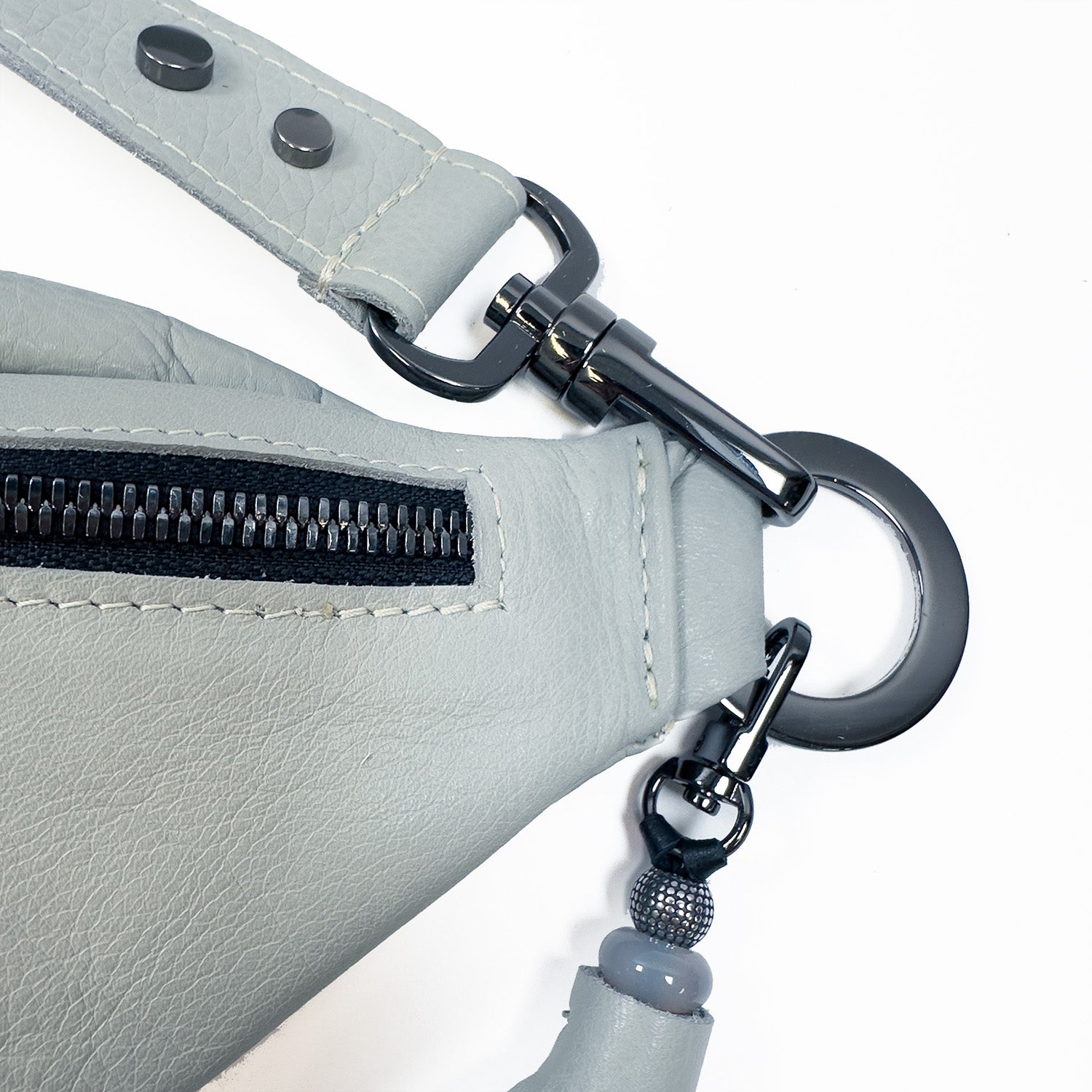 Close-up of the STELLA - light smoke leather sling bag by evokewomen, showcasing a sleek black zipper, metal clips, and an adjustable strap for a perfect fit.