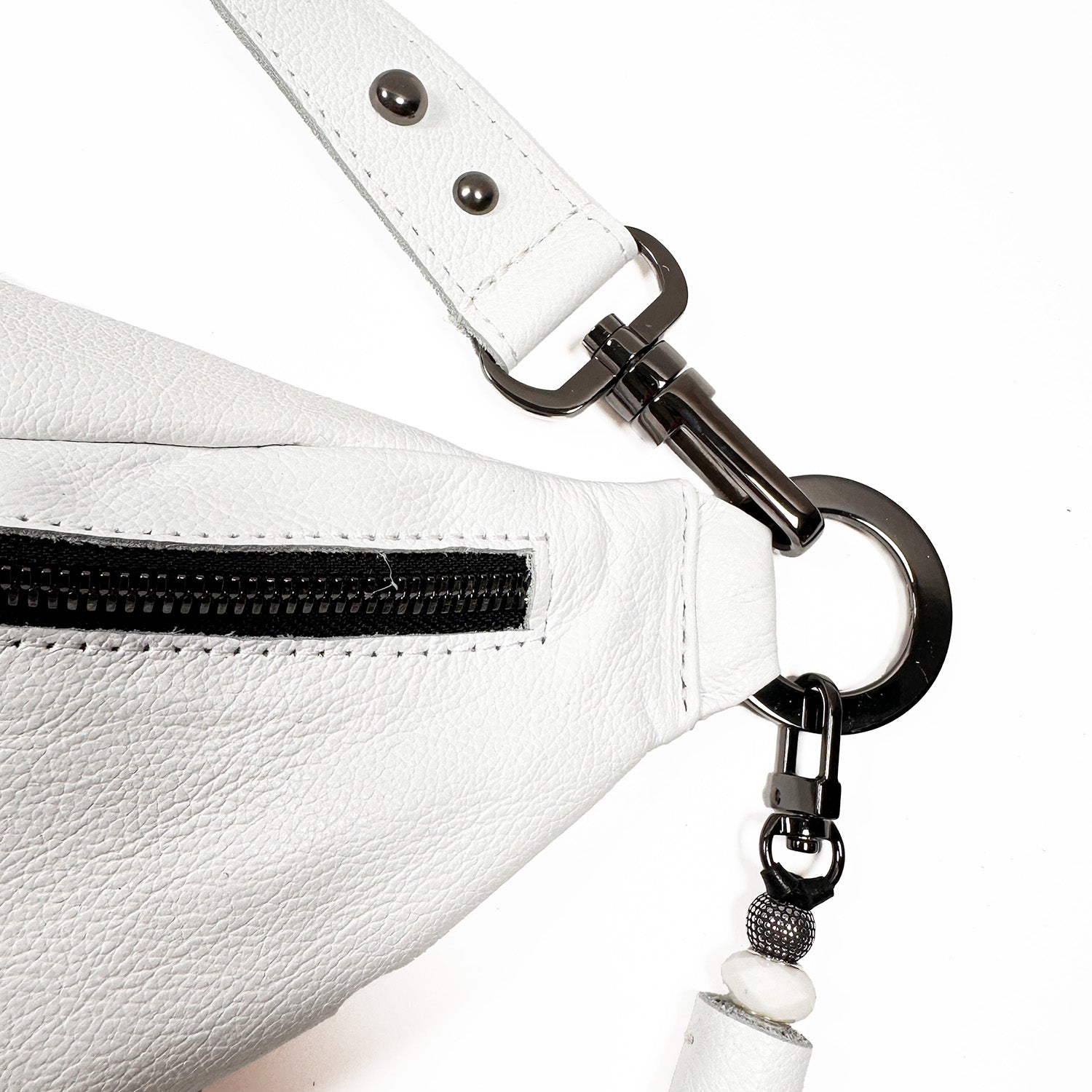 Close-up of the stylish STELLA by evokewomen, featuring a sleek white Italian leather design with a black zipper; adjustable strap adorned with metal ring and clasp details.
