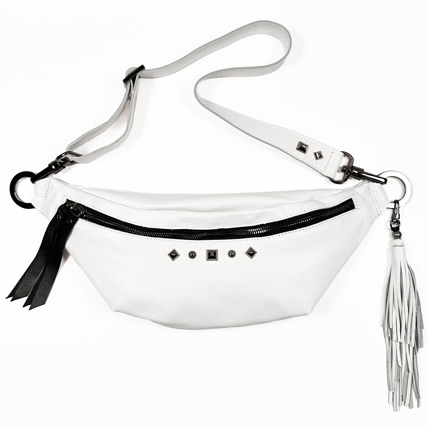 The STELLA by evokewomen is an elegant and versatile white Italian leather crossbody belt bag, adorned with a sleek black zipper, shimmering silver studs, and a chic gray tassel on the side. It is perfect for everyday essentials, combining style and convenience seamlessly.