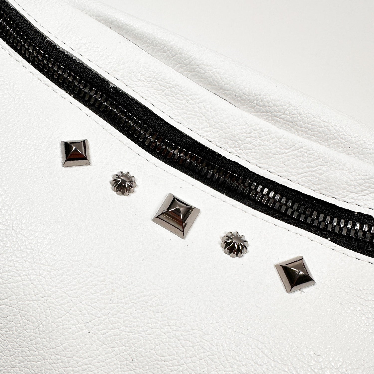 Close-up of the STELLA - white crossbody bag by evokewomen, showcasing its black zipper and silver stud decorations made from Italian leather.