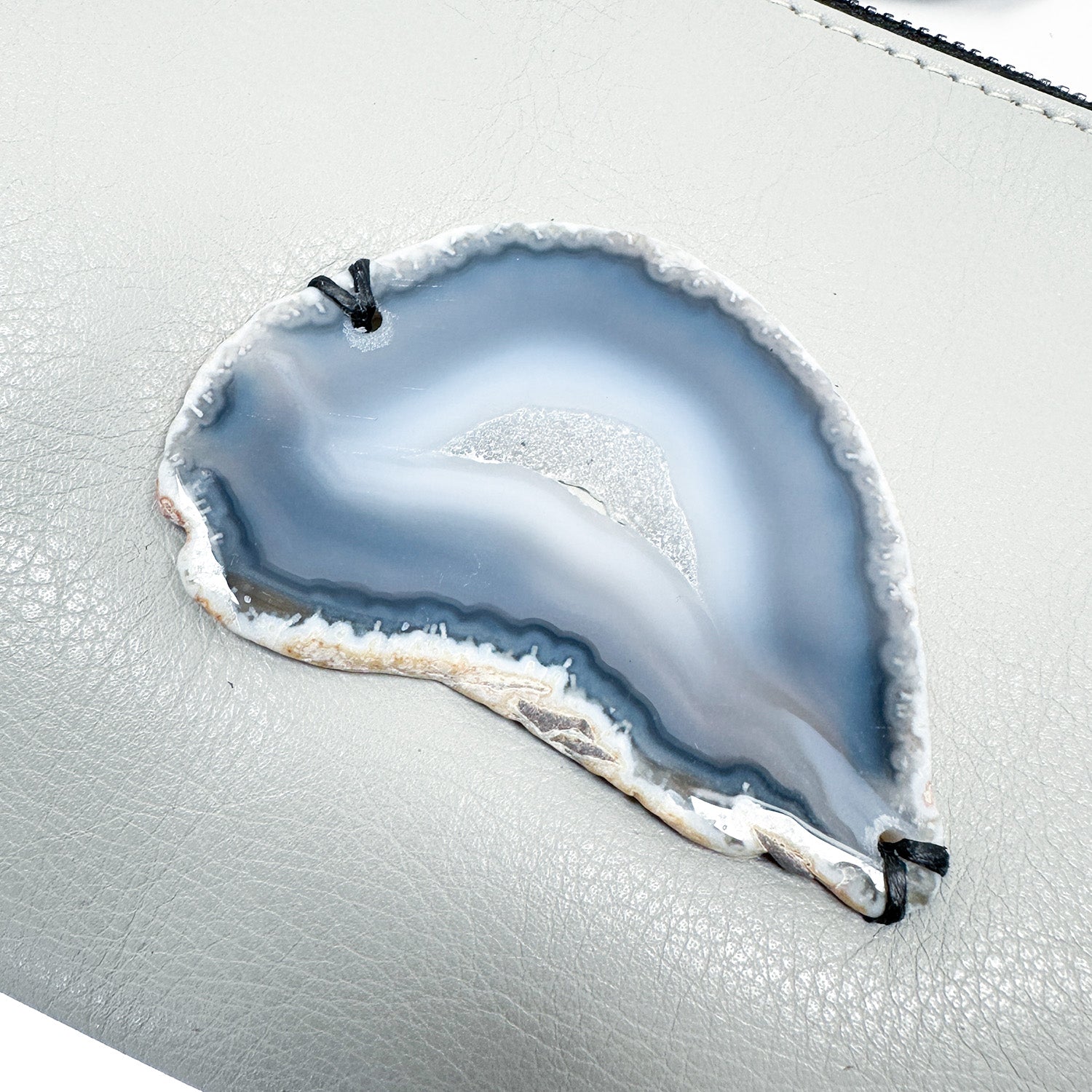 The sophisticated VICTORIA - light smoke clutch from evokewomen features a beautifully sliced agate stone with gray and white bands, elegantly attached to its light gray surface using black ties.