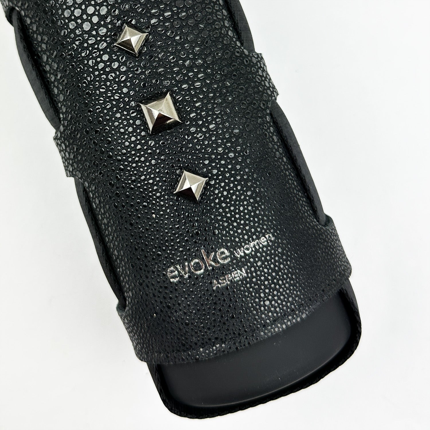 Close-up of a black textured bottle carrier crafted from faux Stingray leather, adorned with metallic studs and the text "evokewomen" imprinted on the strap.