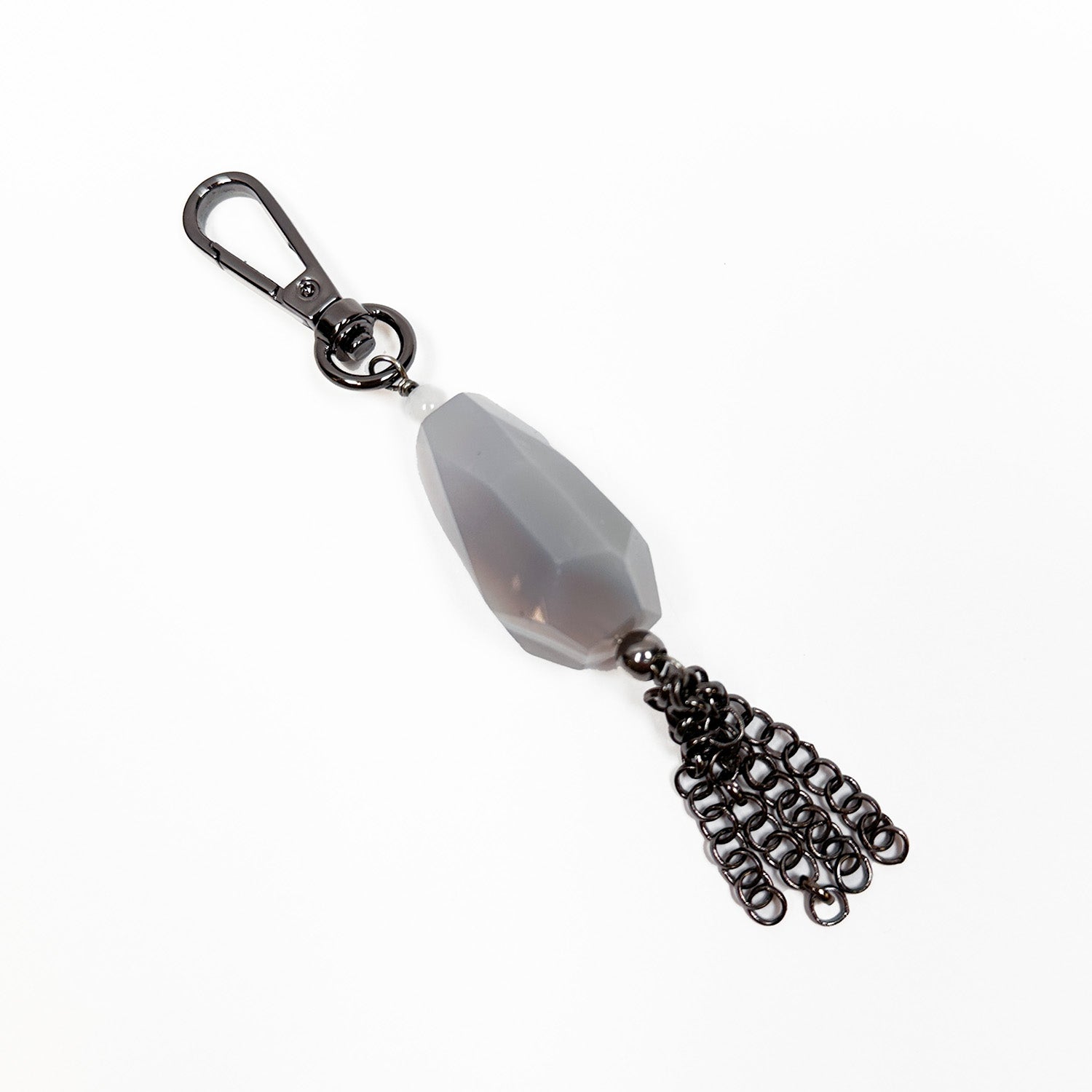 The Teardrop Tassel Charm by evokewomen is a metal keychain adorned with a faceted tear-drop gray stone and decorative chain tassels, set against a white background to beautifully enhance any collection of gunmetal accessories.