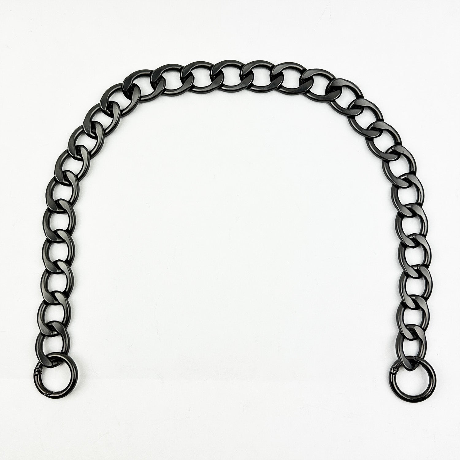 Introducing the LARGE LINK CHAIN - SHOULDER LENGTH by evokewomen, showcasing a gunmetal finish with a striking black metal design. This piece features interlocking round links that elegantly form an arch shape against a crisp white background. Crafted from lightweight aluminium, it promises both durability and comfort for effortless wear.