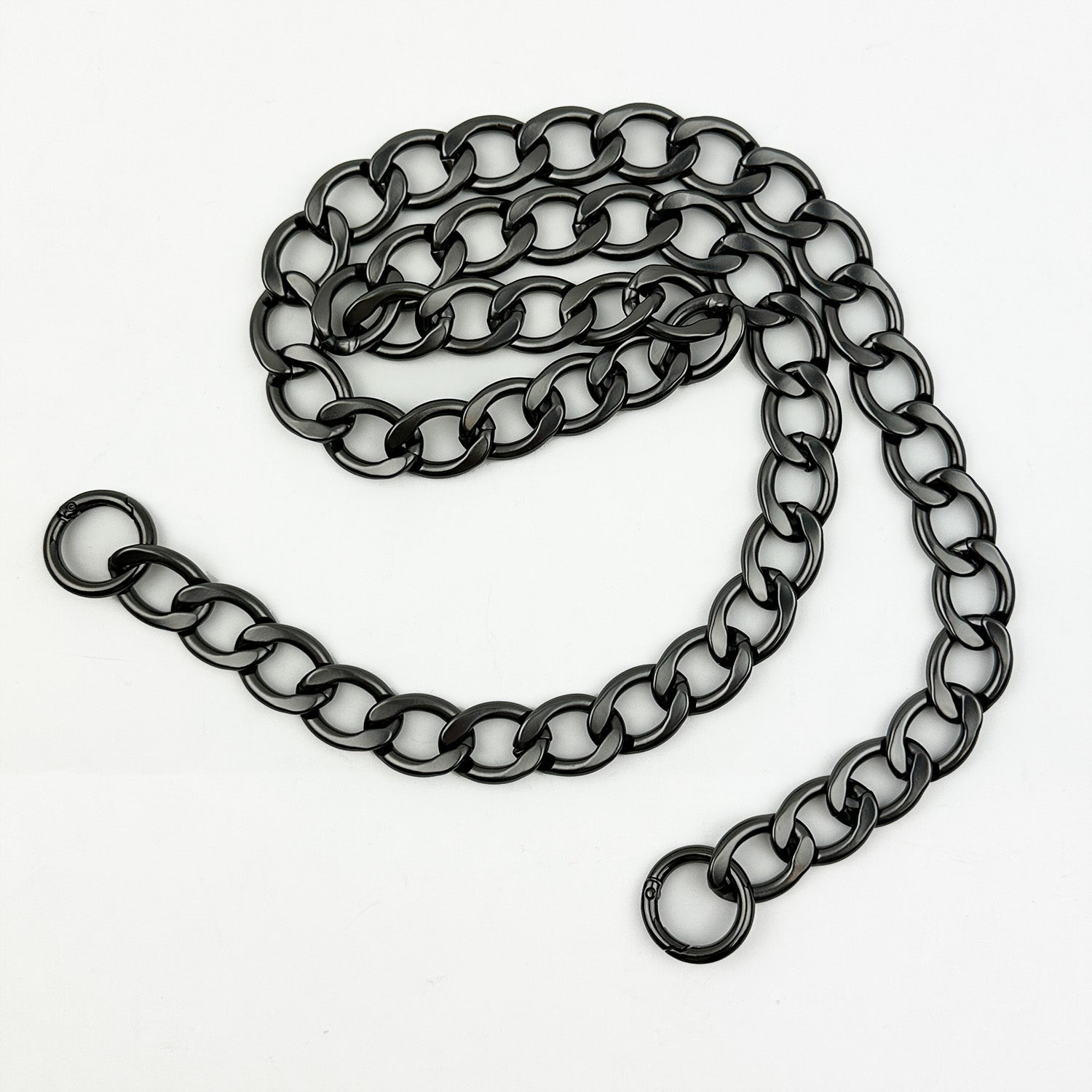 Introducing the LARGE LINK CHAIN - X-BODY LENGTH from evokewomen, a sleek black metal chain featuring large round links arranged in a loose pattern on a white background. Crafted from lightweight aluminum, it boasts an edgy gunmetal finish, making it the perfect striking accessory as a cross-body chain.