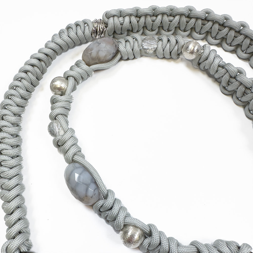 The BAHAMA - LIGHT SMOKE - knotted strap by evokewomen is a rope-like necklace featuring braided gray cords crafted from Italian leather, adorned with beads and stones, displayed on a white background.