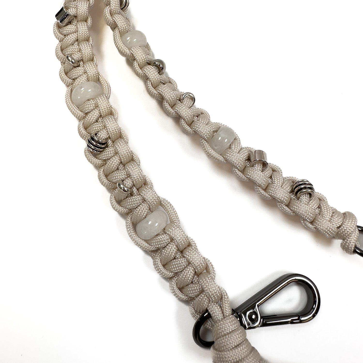 The KNOTTED SHOULDER STRAP - ALMOND by evokewomen is a woven beige paracord strap highlighted with agate beads and gunmetal rings, finished with a metal carabiner clip at the end, displayed on a white background.