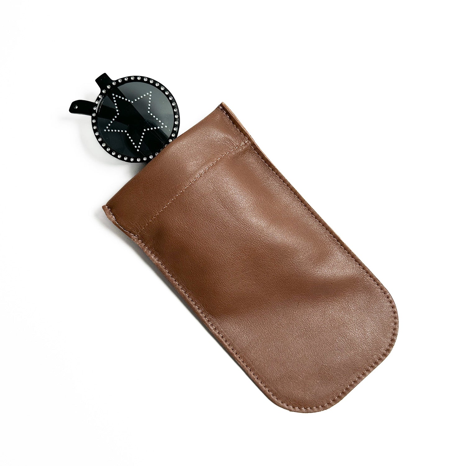 A brown leather sunglasses pouch from evokewomen, known as the SUN-GLASS POUCH - nutshell, features a zipper and partially reveals a black star-patterned circular item inside. Its unique design combines style and functionality seamlessly.