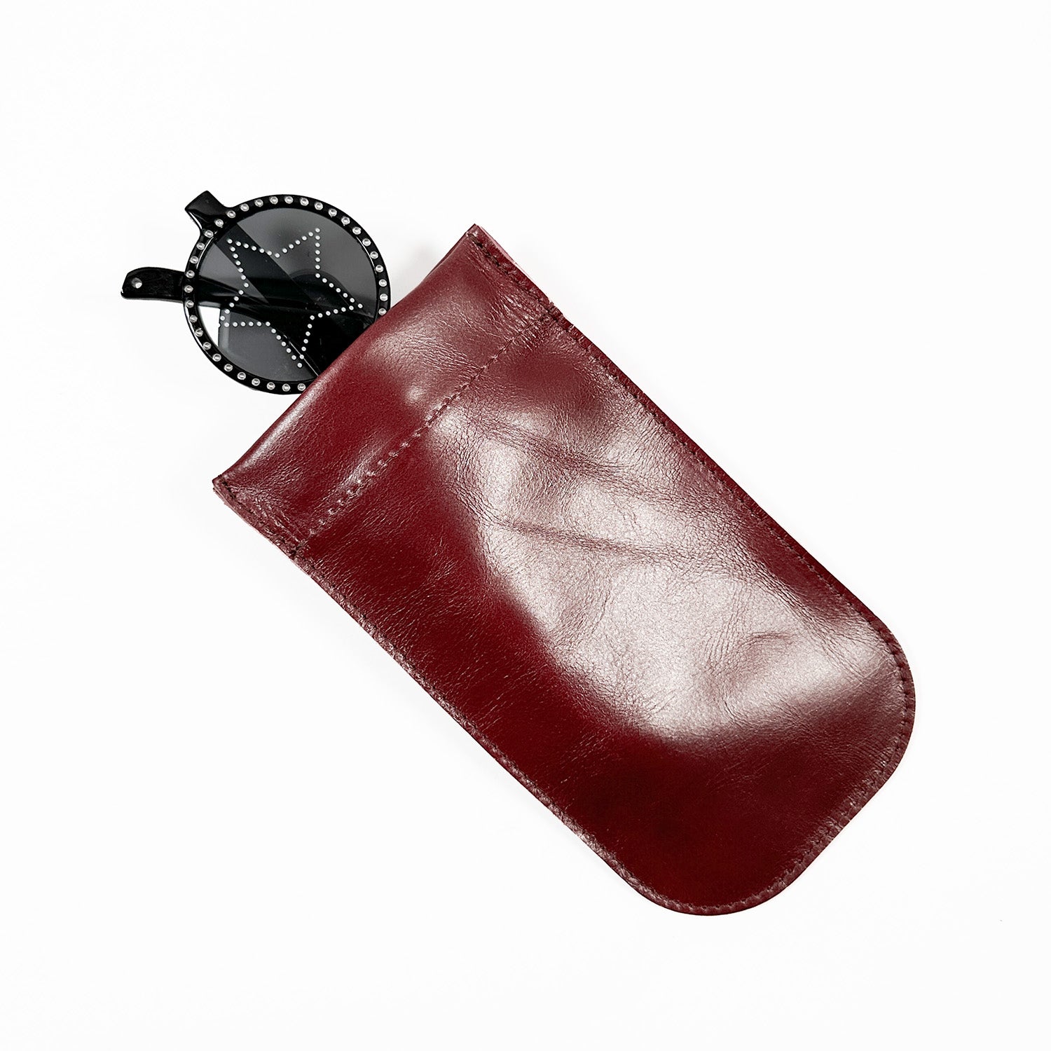 A pair of black round sunglasses peeks out from the evokewomen SUN-GLASS POUCH in a shiny wine hue, showcasing its unique design against a plain white background.
