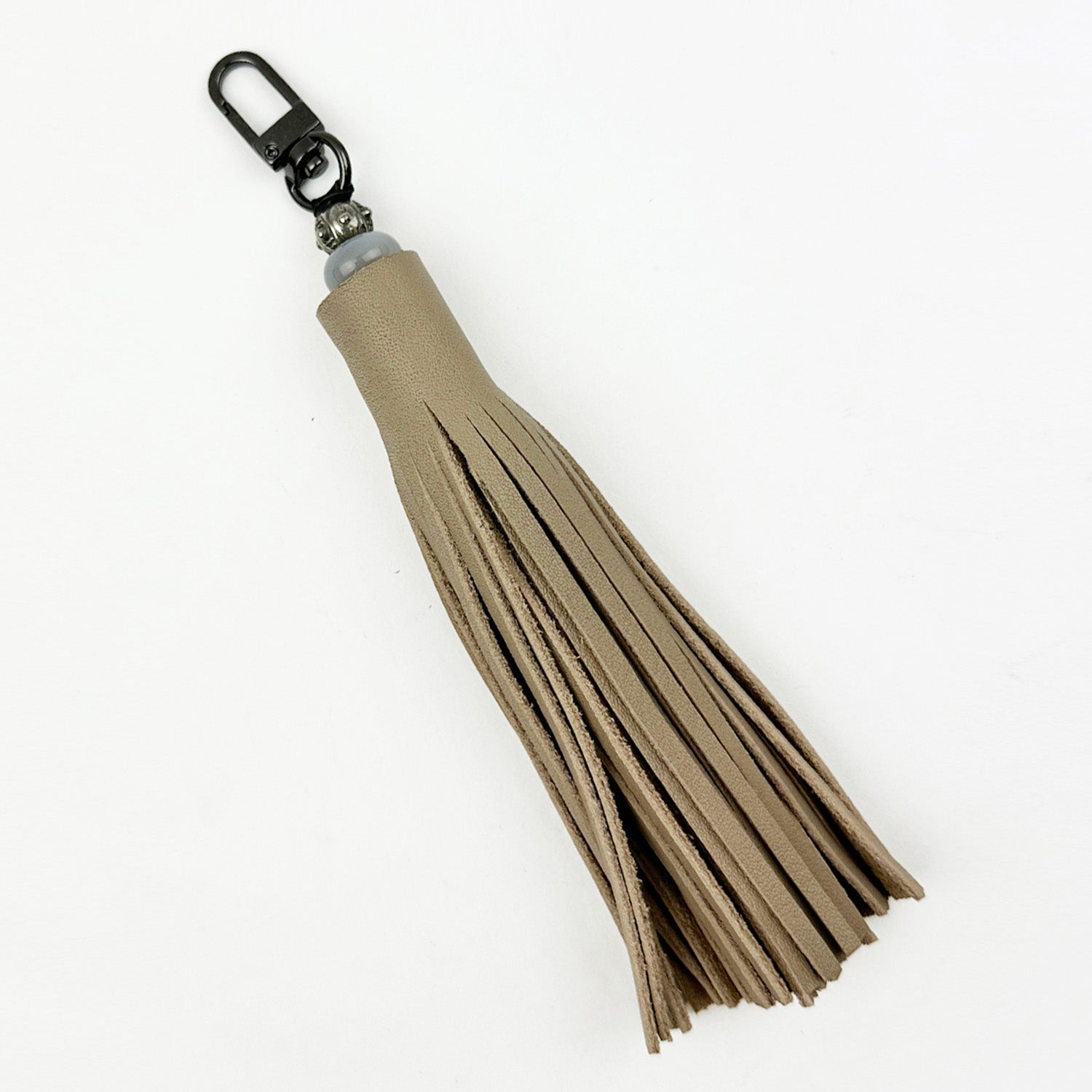 The TASSEL - SAND by evokewomen is a beige leather keychain that exudes fashion magic with its distinctive tiered fringe details and a gunmetal clasp.