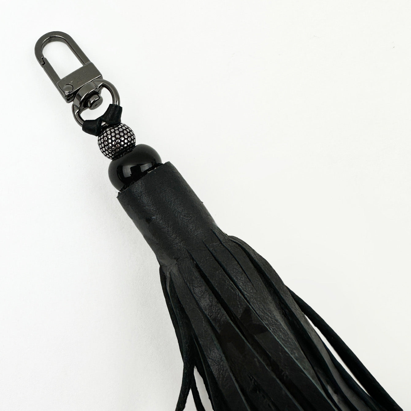 Close-up of the TASSEL - BLACK STARS keychain by evokewomen, showcasing a black leather tiered tassel with a gunmetal swivel hook, bead, and fringe.