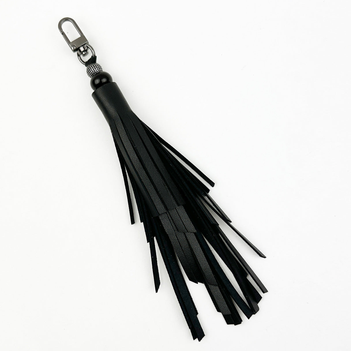 Introducing the TASSEL - BLACK by evokewomen, a distinctive black leather fringe keychain featuring a unique tiered tassel design and a gunmetal swivel hook.