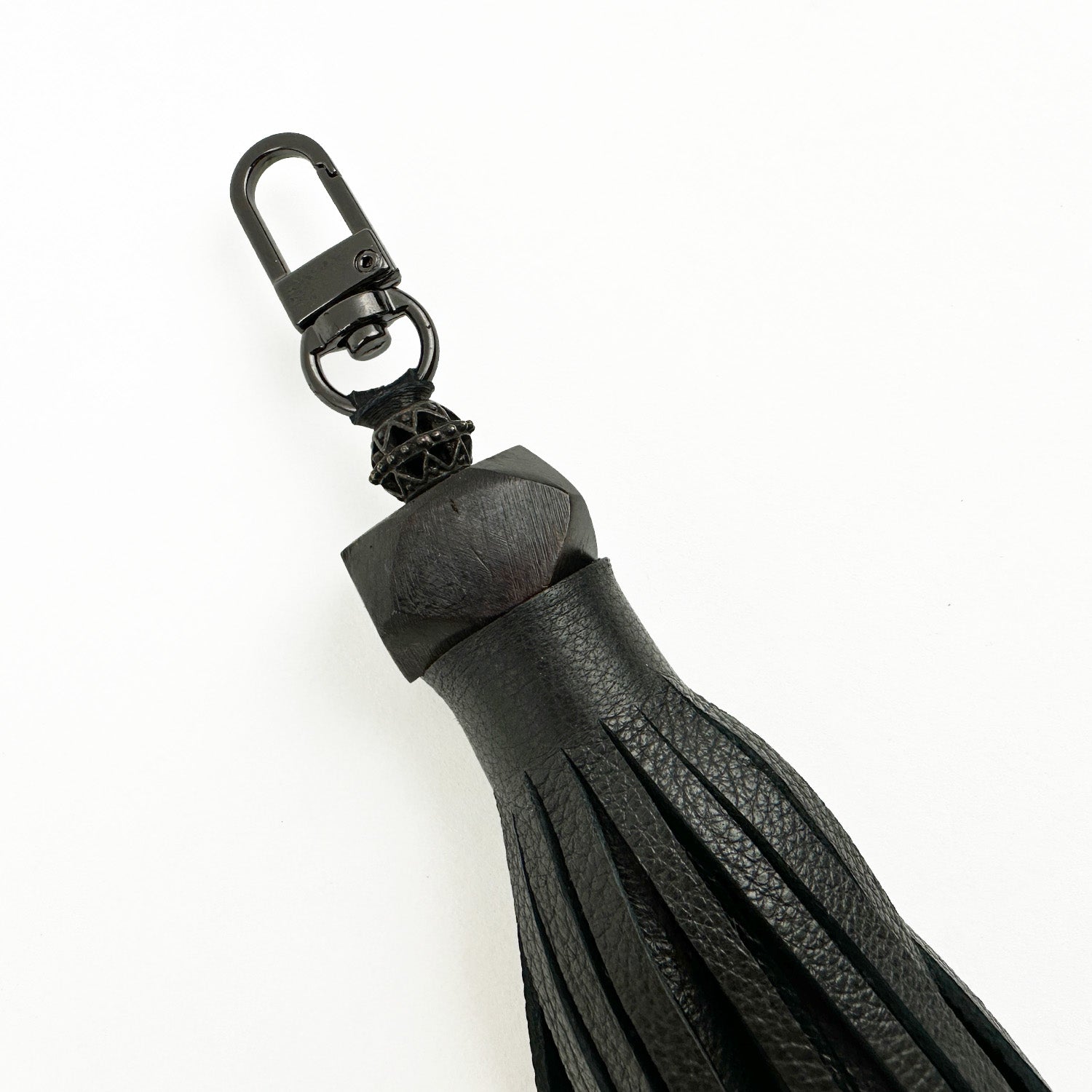 The TASSEL - BLACK LARGE by evokewomen is a black leather keychain featuring a gunmetal clasp, fringed edges, and a decorative knot. This elegant accessory enhances any set of keys with a touch of sophistication.