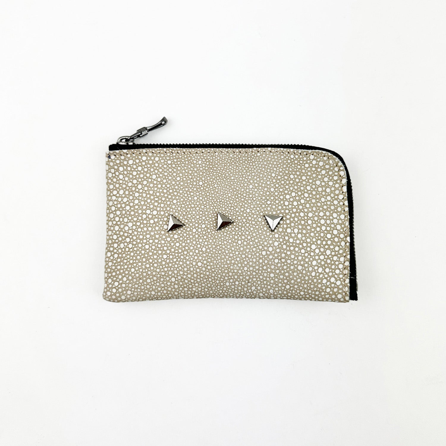 The MINI WALLET - STINGRAY SAND by evokewomen is displayed against a white background, highlighting its small textured beige leather design with three triangular silver studs and a black zipper.