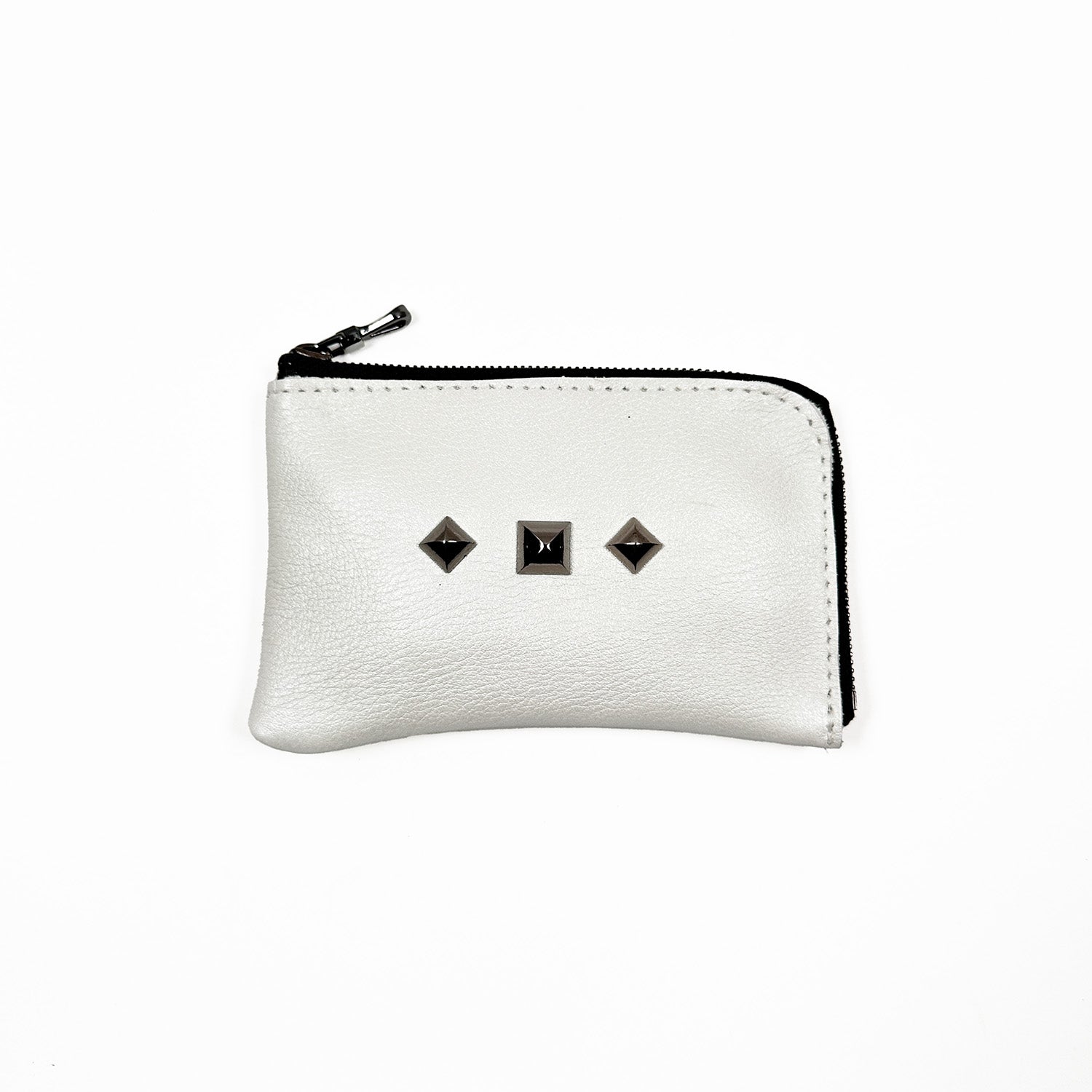 The MINI WALLET in pearl white by evokewomen is a small leather zippered pouch with a distinctive design featuring three square metal studs on the front.