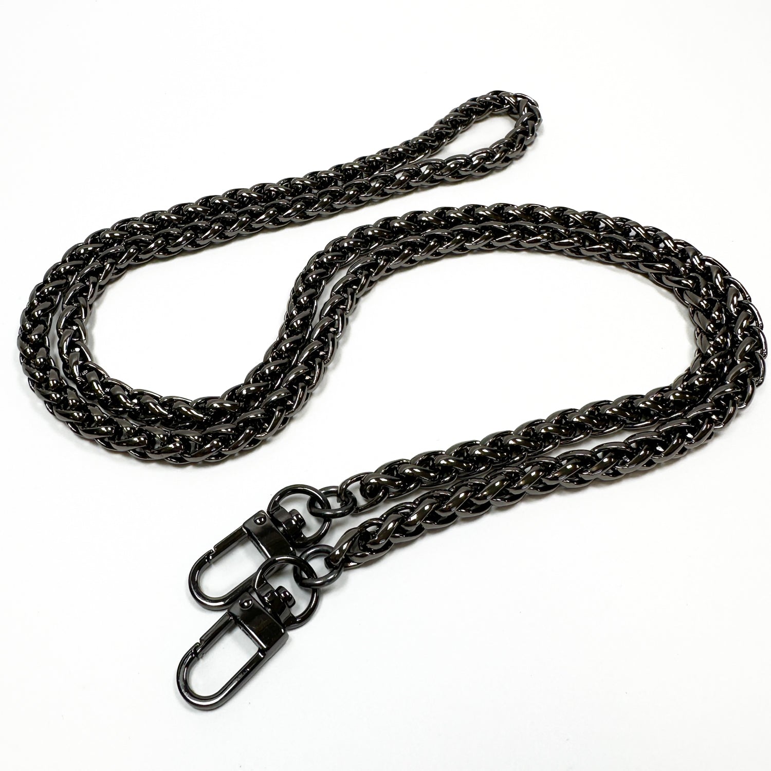 A lengthy, sleek chain in a deep metal finish, reminiscent of a snake spine chain, showcases clasps at both ends and is artfully arranged in a loose and elegant form on a white background. This piece is the Farah - wine by evokewomen.