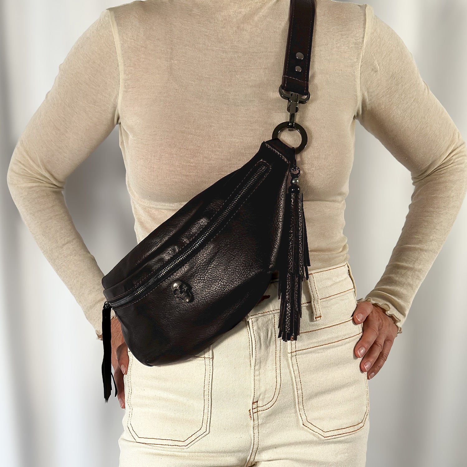 A person wearing a beige long-sleeve top and light jeans is posing with the STELLA - BROWN Italian leather shoulder bag from evokewomen, featuring subtle skull decorations.