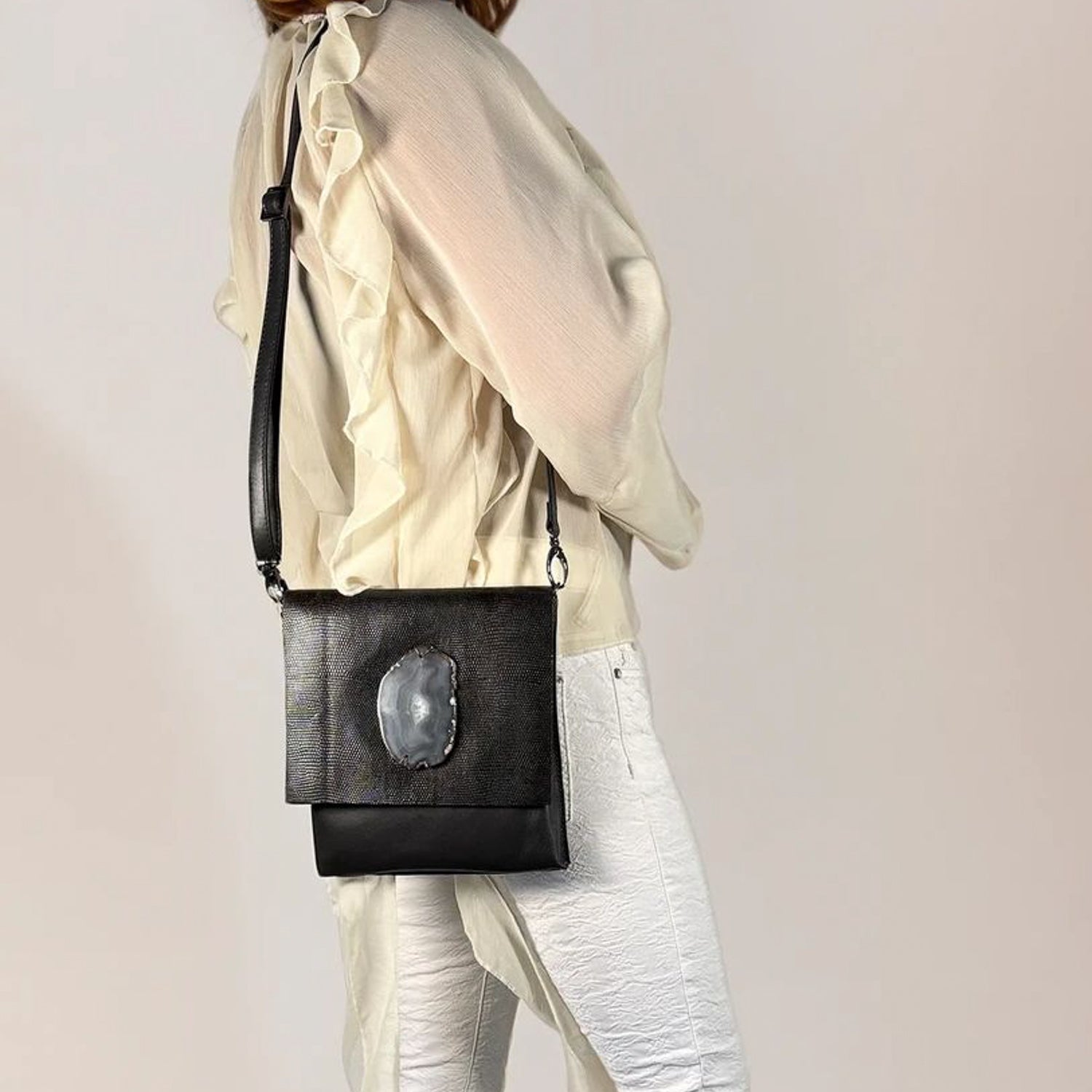 Person wearing a dark brown crossbody bag with a unique design on a plain background