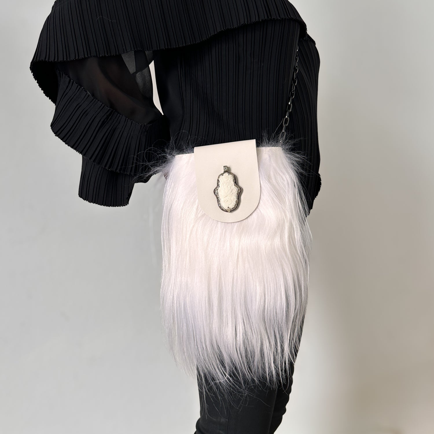 A person dressed in a black pleated top and pants carries the MIA - WHITE handbag from evokewomen, exuding chic elegance with its versatile design and stylish metal embellishment.