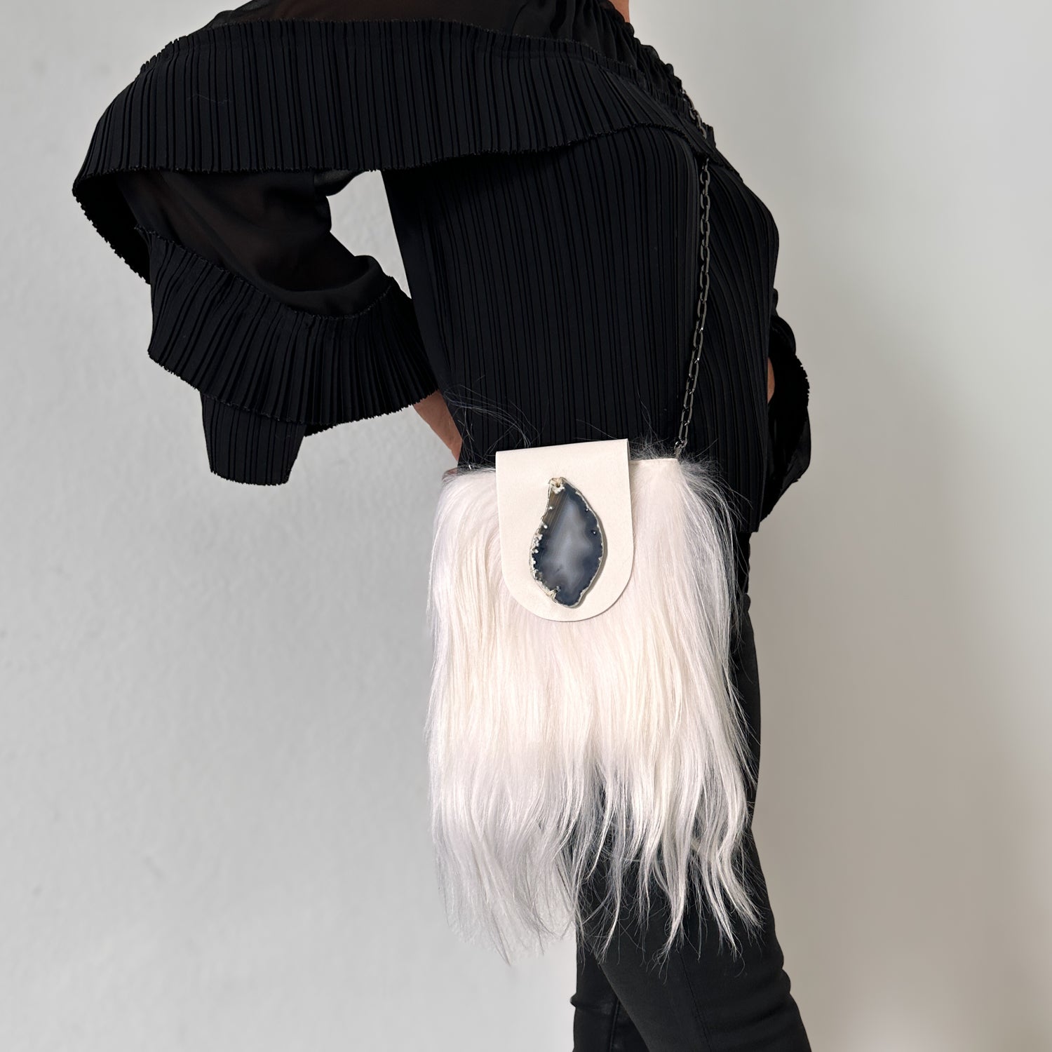 Person in a black pleated outfit carrying the MIA - WHITE crossbody bag by evokewomen, featuring striking white fur and a geode accent.