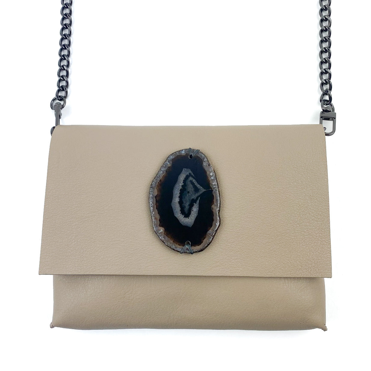 The BAHAMA - SAND by evokewomen is a beige leather cross body bag that boasts a refined chain strap and a striking central black geode accent on the flap.