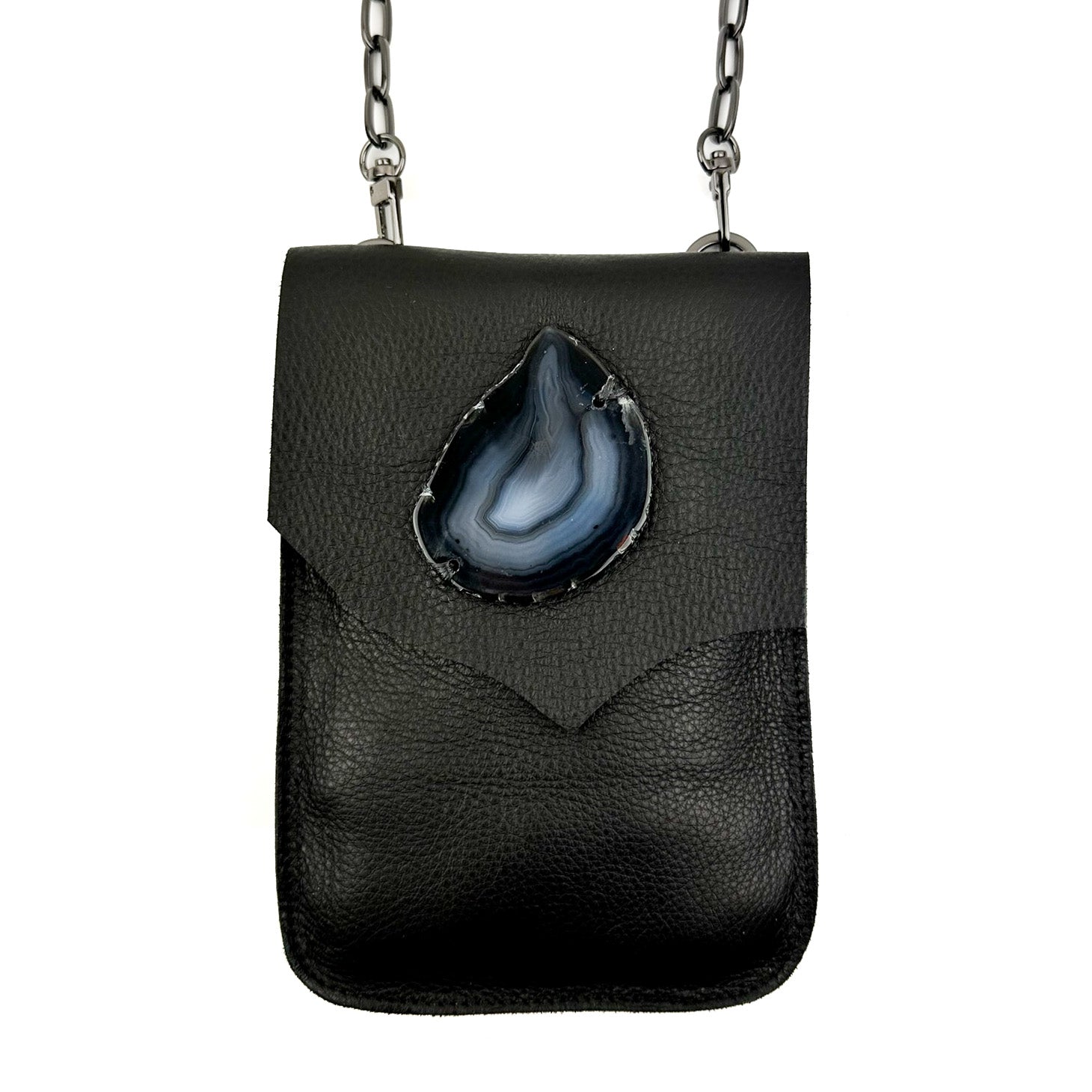 Introducing the PAULINA - BLACK by evokewomen: a sophisticated crossbody bag crafted from elegant black Italian leather. It features a striking tear-shaped blue agate stone on the front and is finished with a stylish silver chain strap. This chic accessory also includes a convenient magnetic closure for secure carrying.