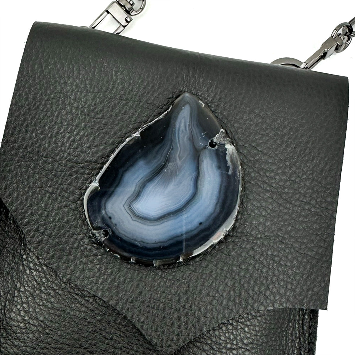 The PAULINA - BLACK by evokewomen is an exquisite black Italian leather cross body bag, designed with a flap and highlighted by a teardrop-shaped agate stone accent in shades of grey and white, secured at the center with a magnetic closure.