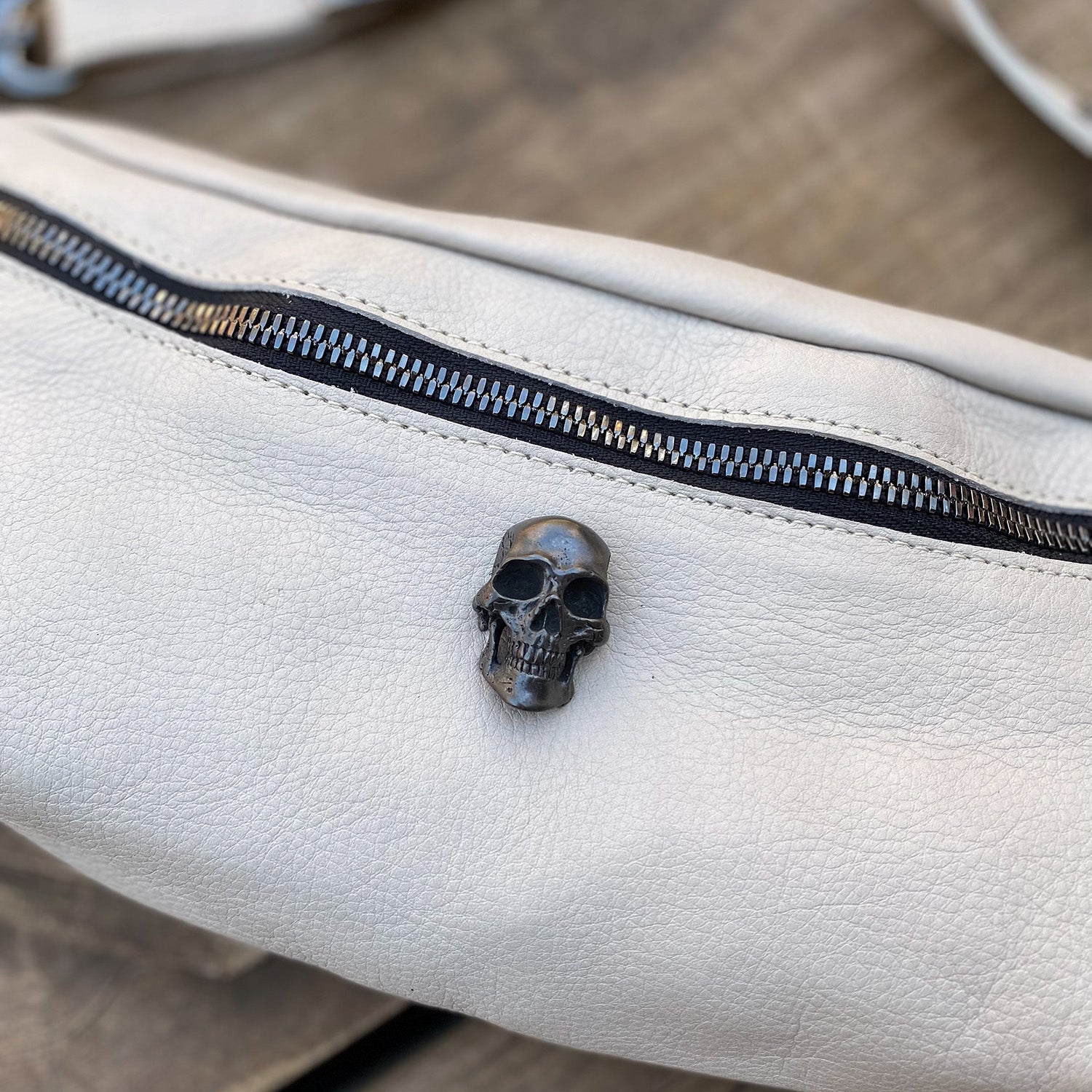 STELLA - PUTTY from evokewomen is a white leather crossbody bag with a black zipper and a small black skull embellishment on the front.