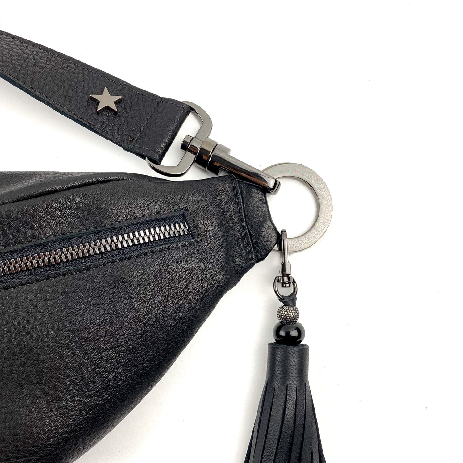 Close-up of the STELLA - BLACK leather crossbody bag by evokewomen, showcasing a star embellishment on the strap, a zipper, and a tassel keychain attached to a metal ring.