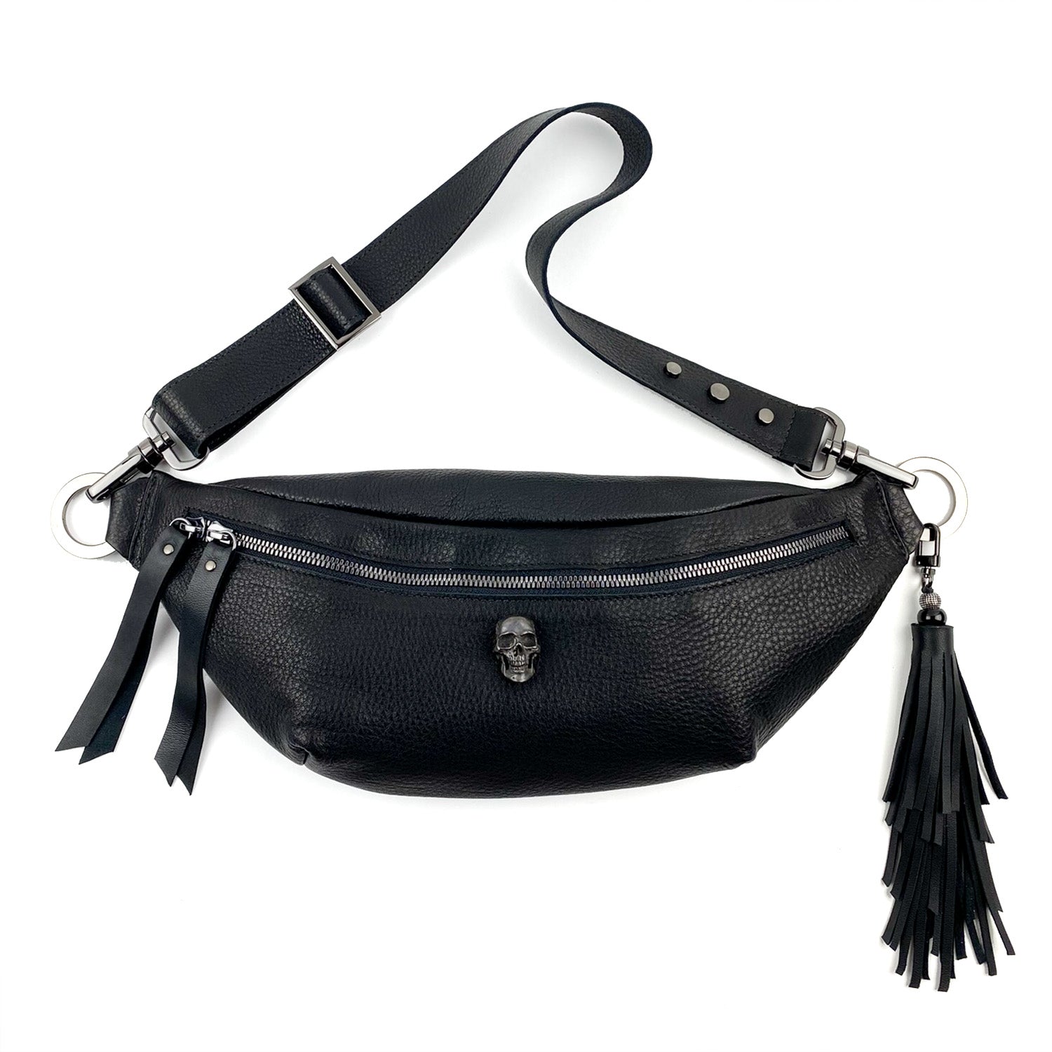 The STELLA - BLACK by evokewomen is a black leather crossbody bag featuring a skull emblem, front zipper, adjustable strap, and a tassel accent on the side.