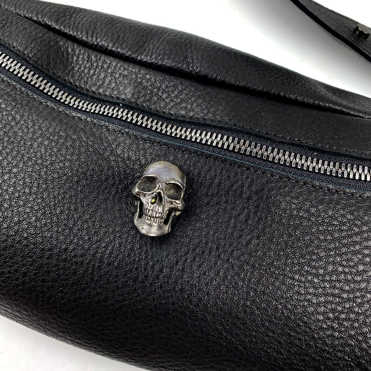 Introducing the STELLA - BLACK by evokewomen, a sleek black leather sling bag adorned with a striking silver skull zipper pull.
