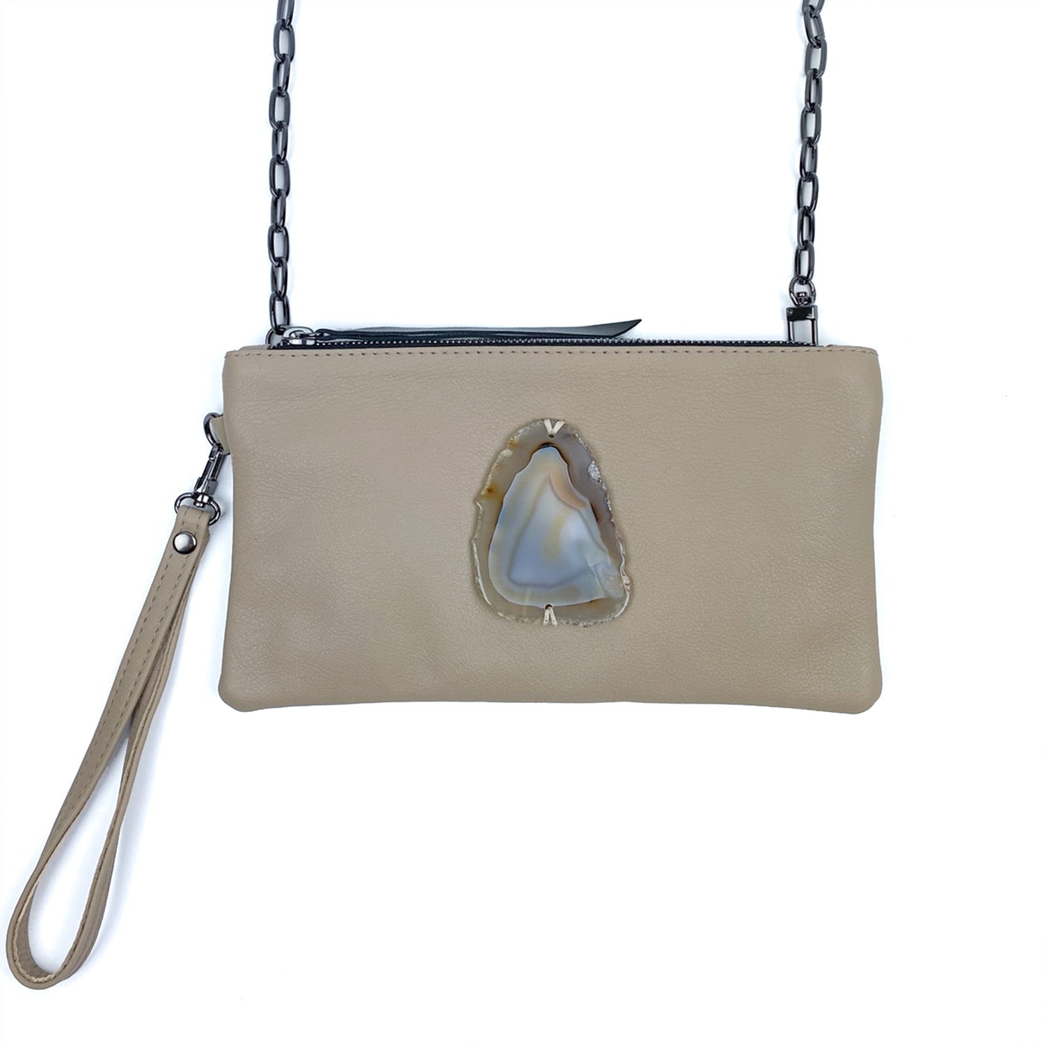 The VICTORIA - SAND by evokewomen is a beige leather crossbody bag with a wrist strap, beautifully combining the elegance of a wristlet and the practicality of a clutch, and adorned with an agate stone embellishment at its center.