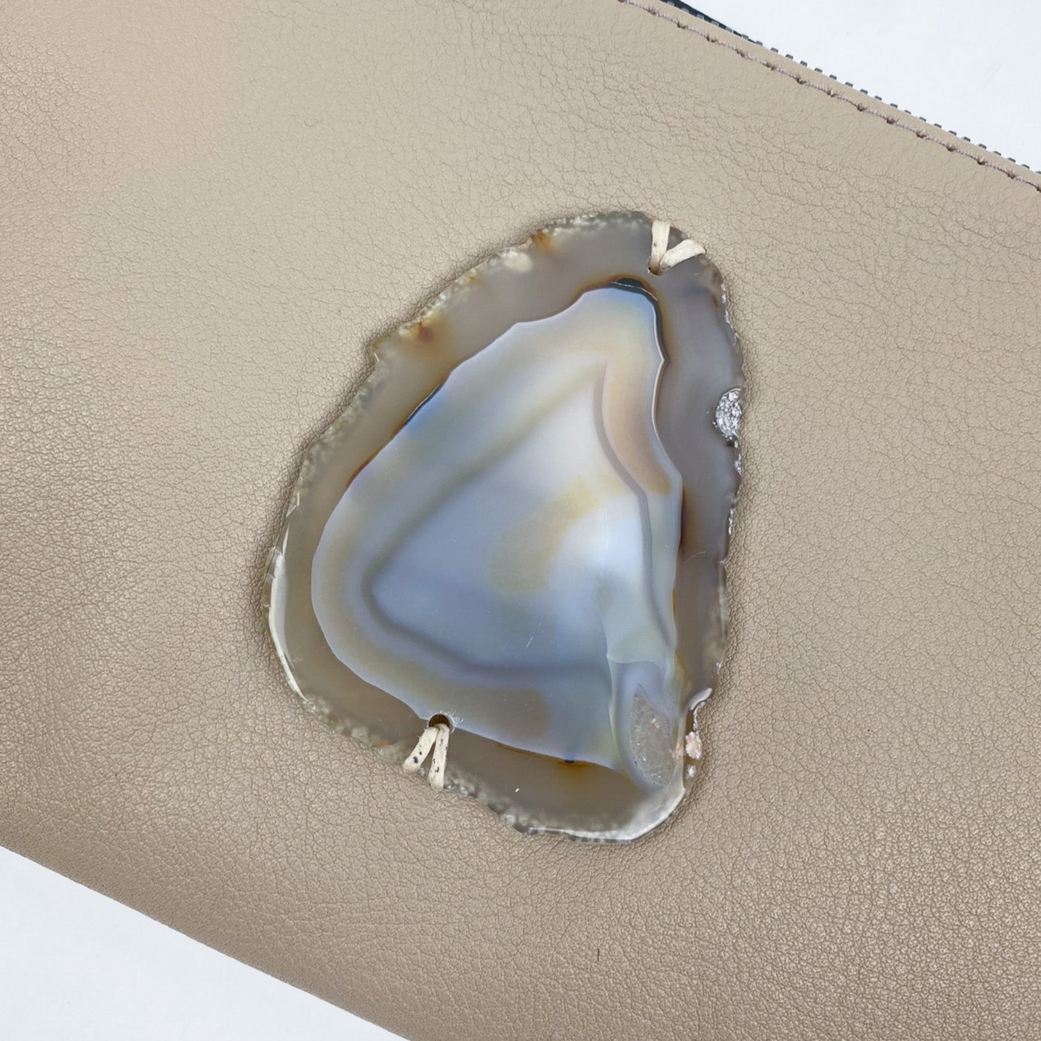 The VICTORIA - SAND clutch by evokewomen features a natural agate slice embedded in a beige, textured leather material, adding an elegant touch to this versatile accessory.