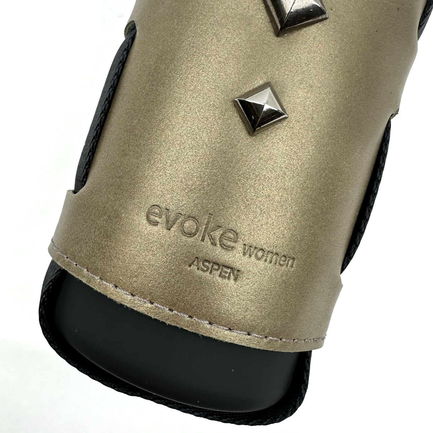 A bottle carrier in bronze from evokewomen, featuring pyramid-shaped rivets and embossed text, adds a touch of edgy sophistication.