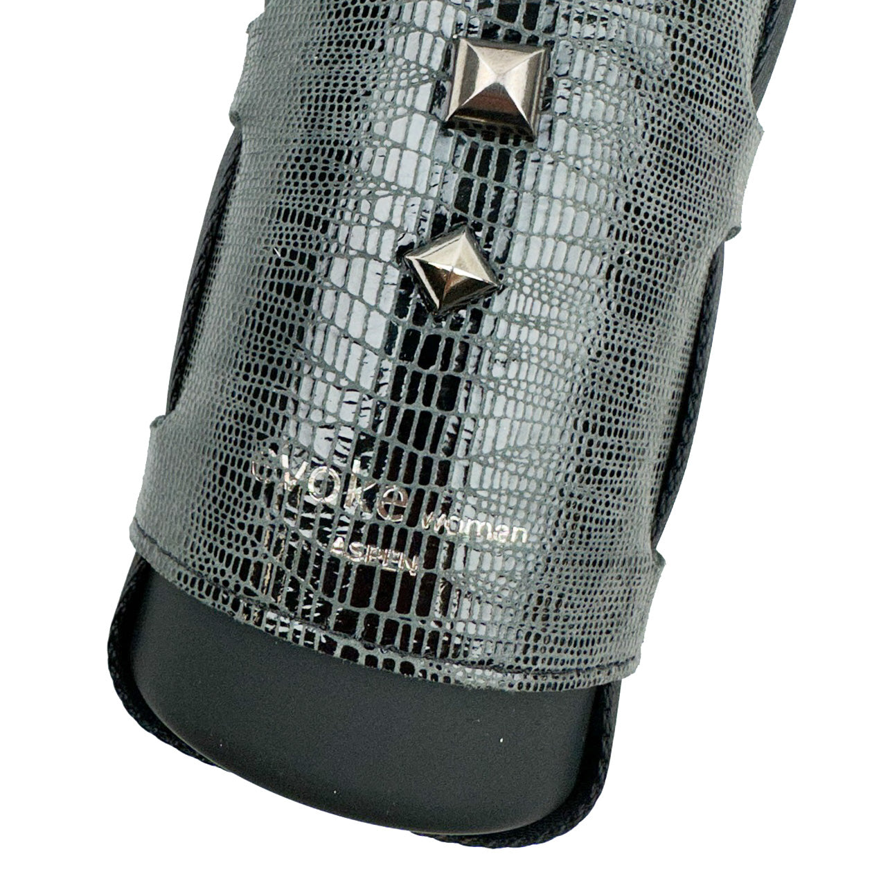 A close-up of a black textured Bottle Carrier by evokewomen, designed in faux snake leather and adorned with silver square studs, with the word "Wom" partially visible.