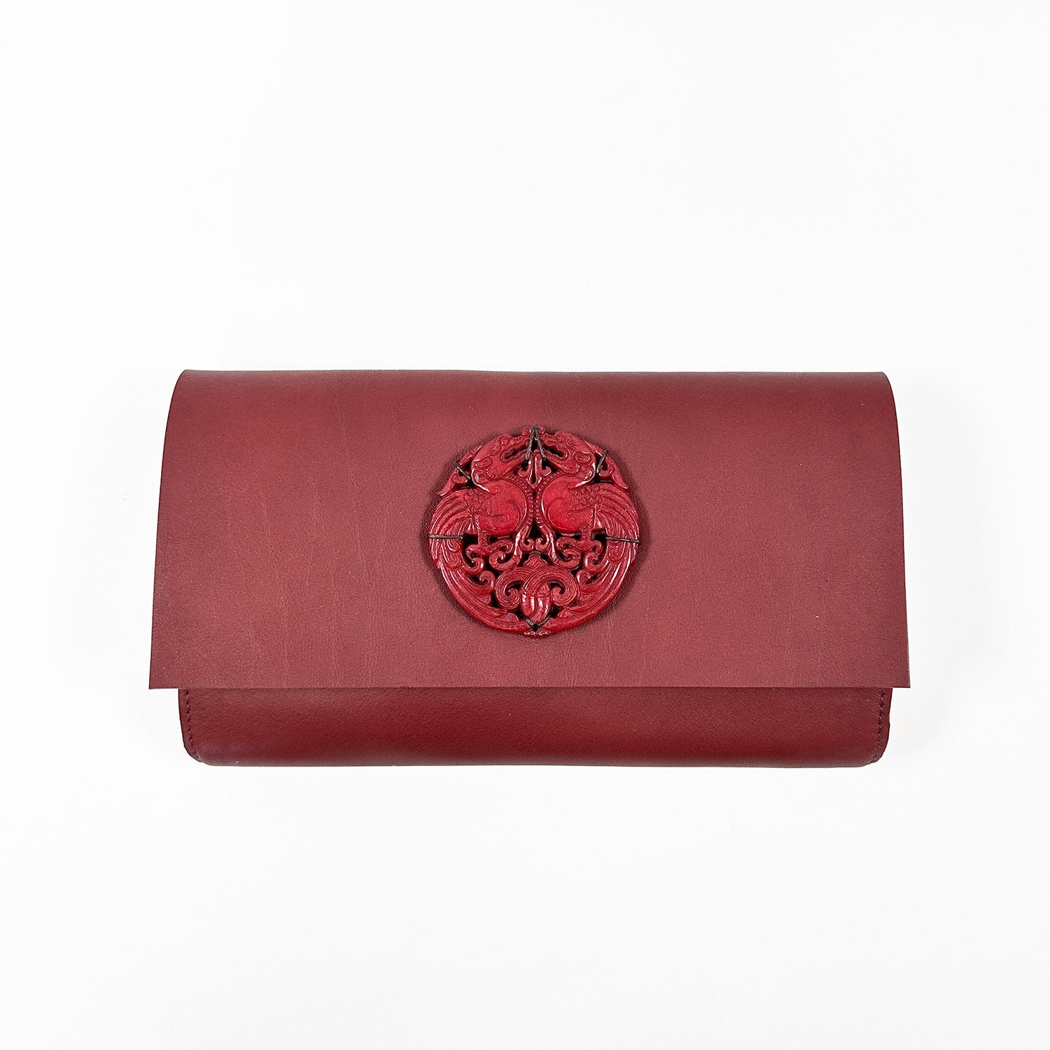 The BAGUETTE - WINE by evokewomen is an Italian leather baguette clutch in a rich brown hue, adorned with an elegant circular emblem on the front flap.