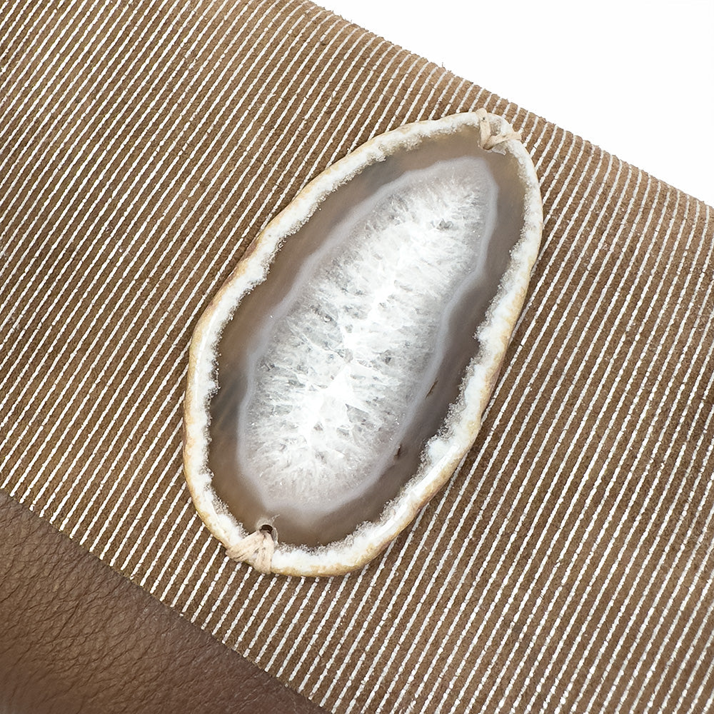 Close-up of the BAHAMA - nutshell-silver by evokewomen, featuring a sliced geode with a crystal interior, placed on a striped fabric surface reminiscent of Italian leather texture.