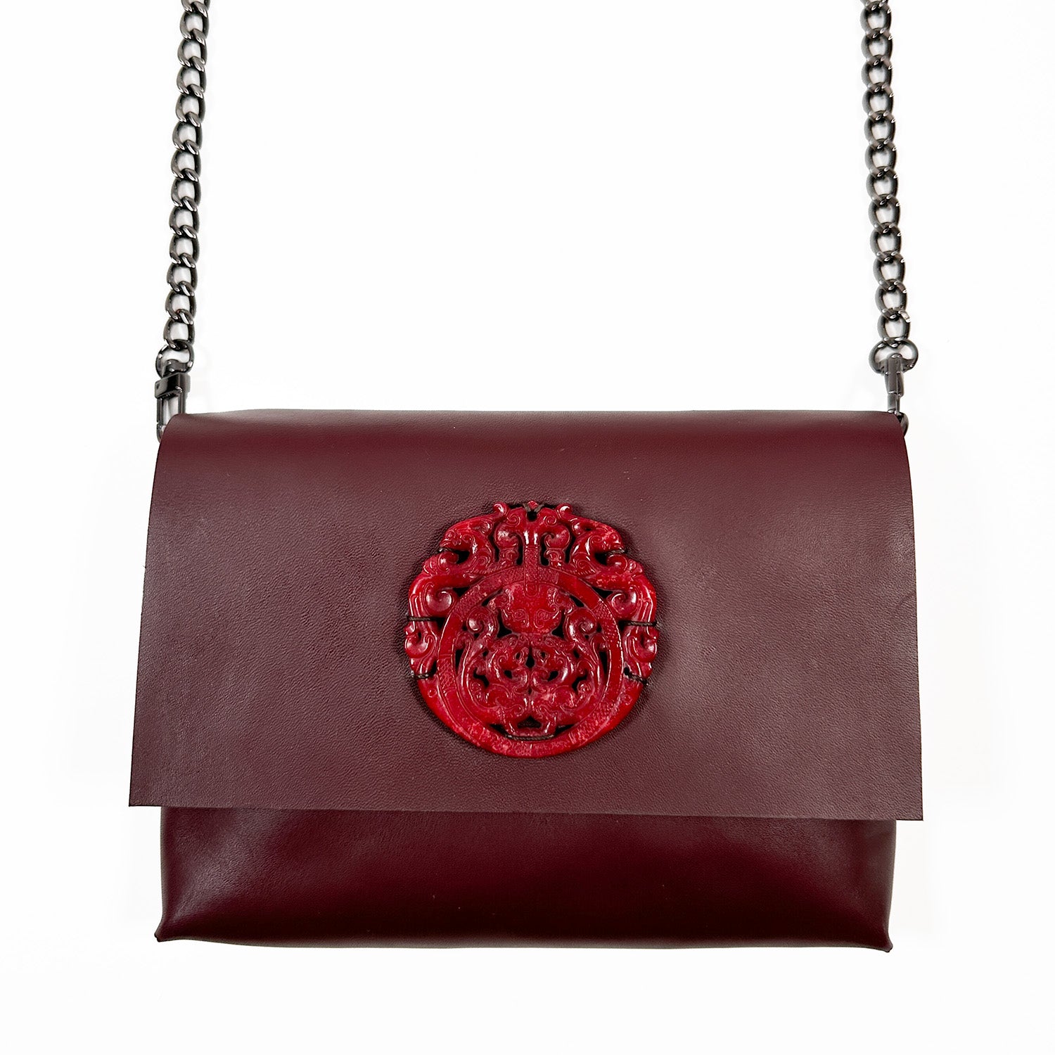 Introducing the BAHAMA - burgundy by evokewomen, an exquisite Italian leather handbag in a rich dark red, featuring a striking embossed emblem on the flap and complemented by a sleek black chain strap—ideal for sophisticated crossbody wear.